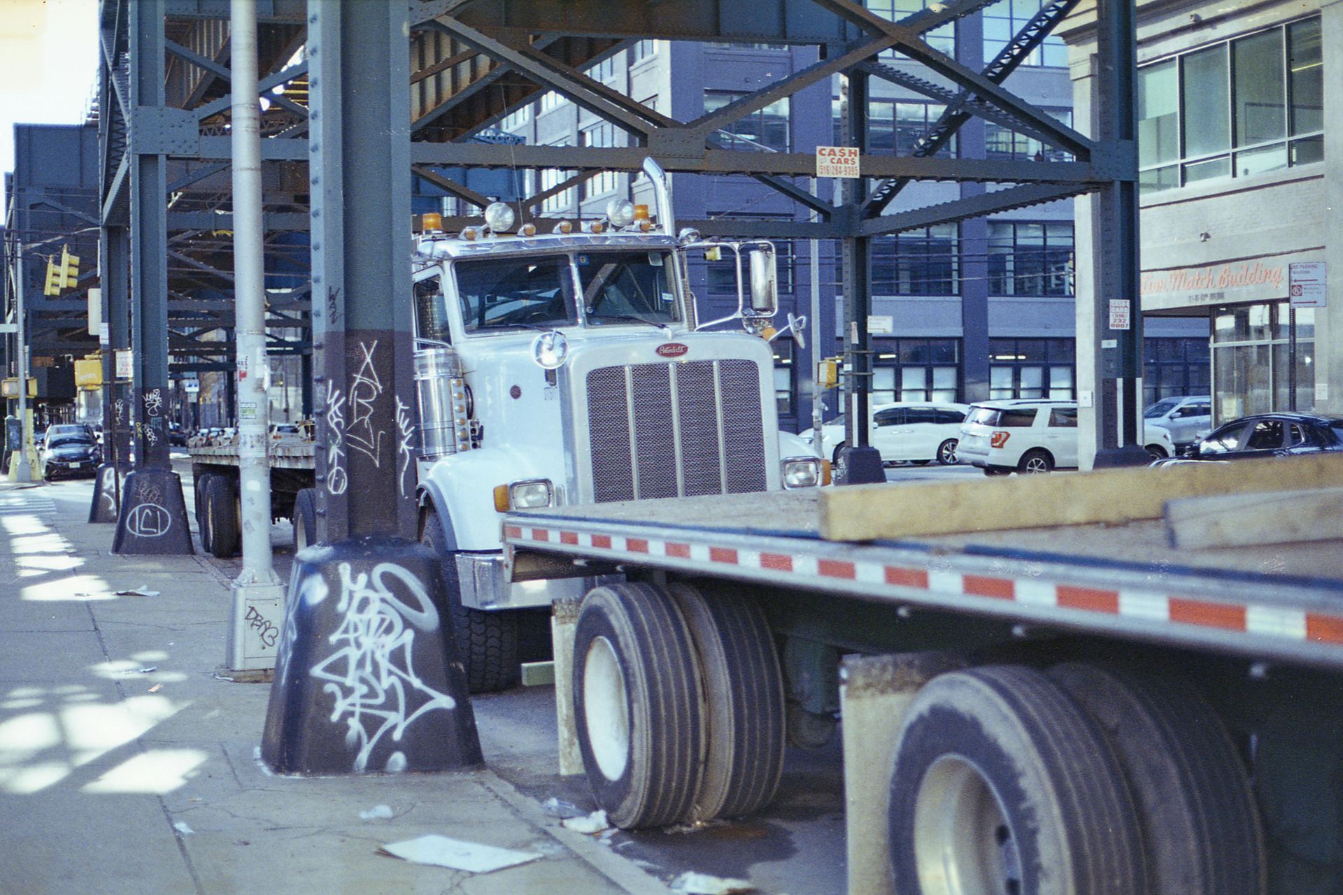 White semi-truck parked under an elevated train structure on a city street.