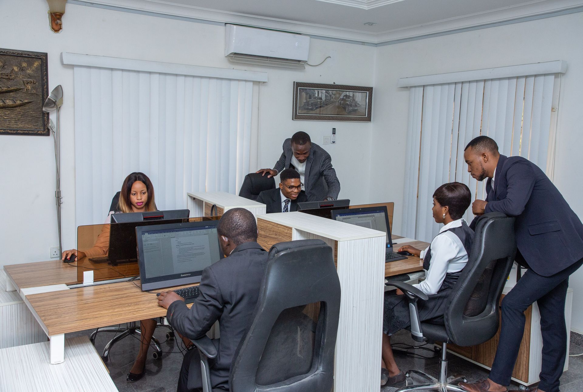 Office meeting around desks with laptops, people discussing documents in a bright room.