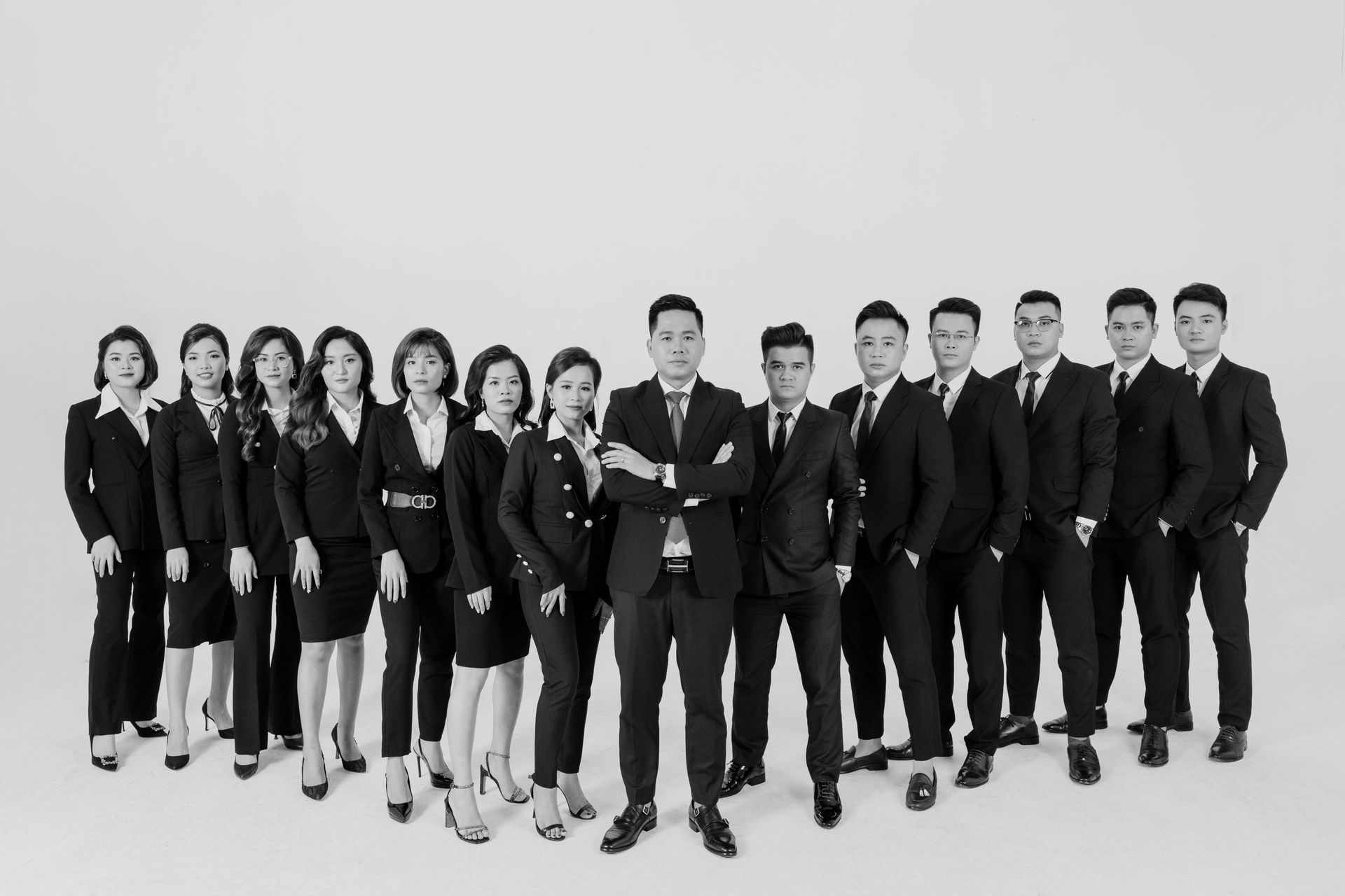 A group of fifteen people in formal business attire pose standing in a line against a plain white background.