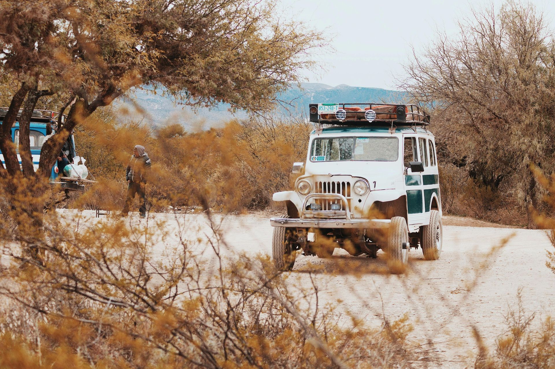 A white jeep is driving down a dirt road in the desert.