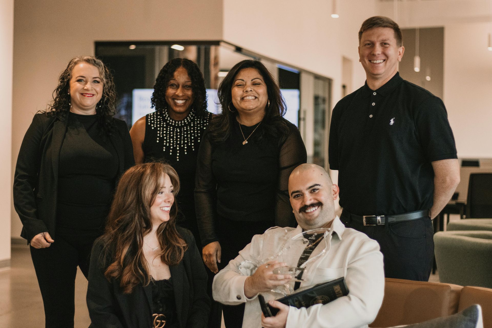 Six professionals smiling at camera in an office setting.