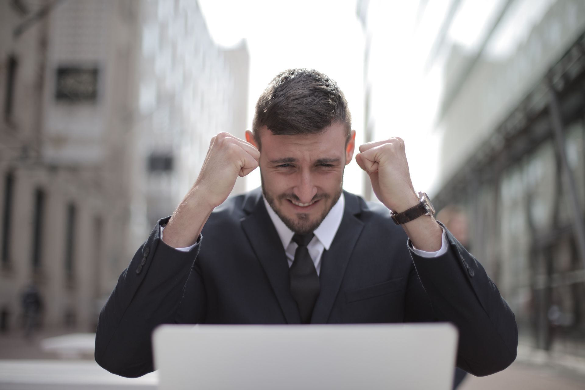 Businessman celebrating with raised fists behind a laptop in a city street