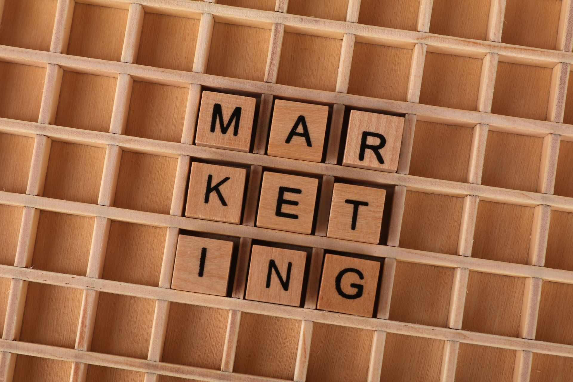 Wooden letter tiles spelling “MARKETING” on a lattice-patterned board.