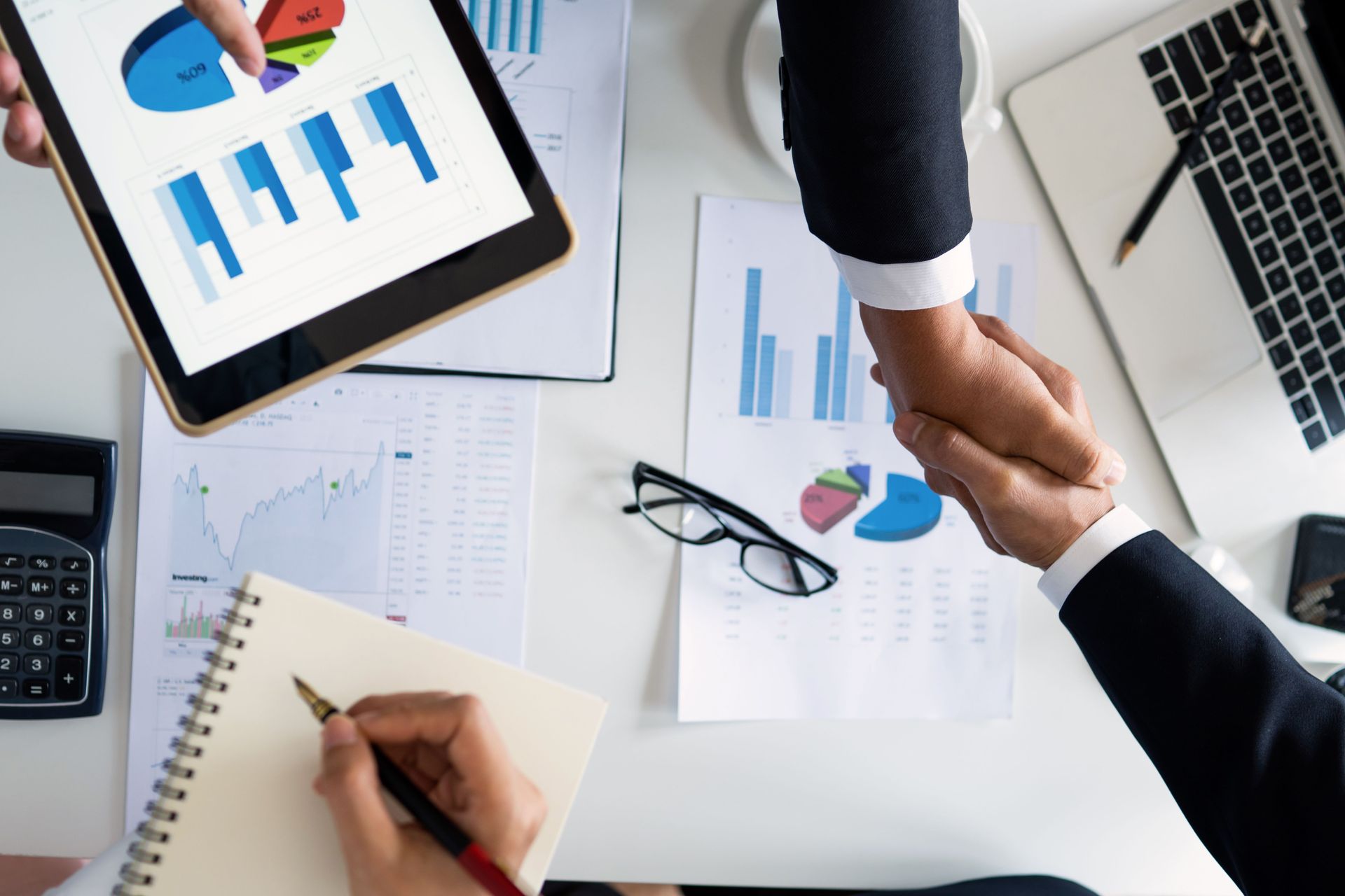 Business meeting with a handshake over charts and reports on a desk