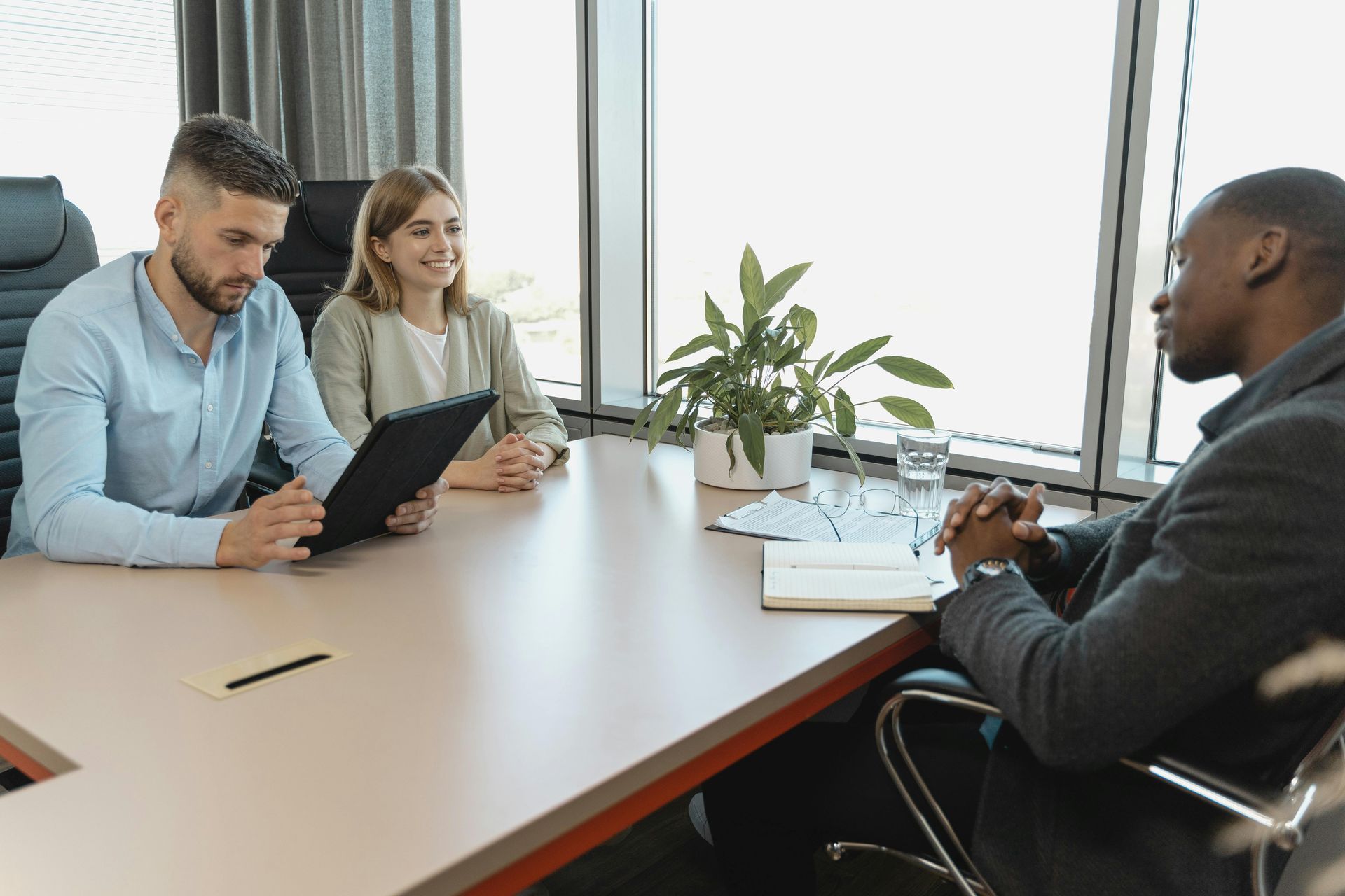 A professional job interview in a bright, modern office with two interviewers and one candidate at a conference table.