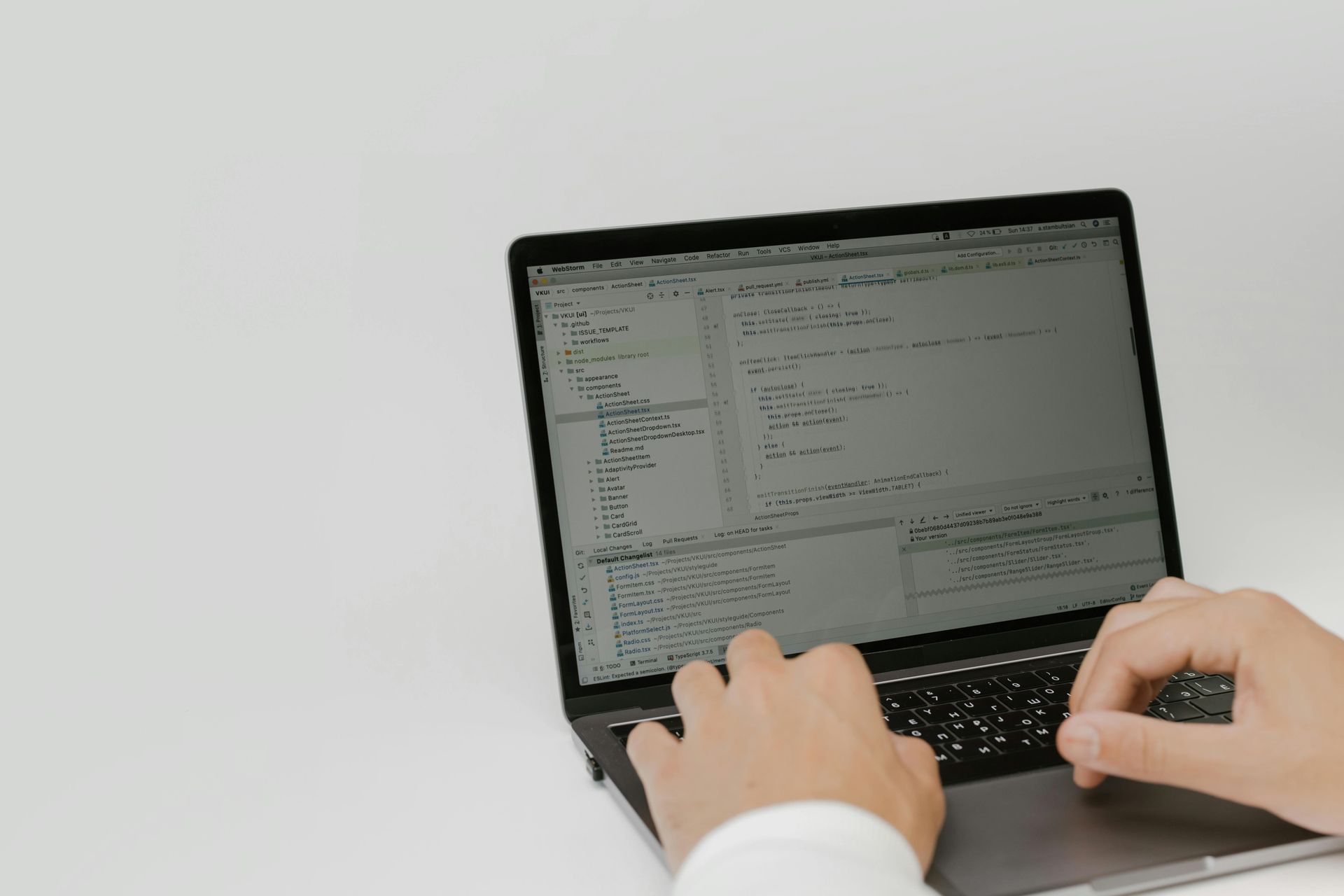 Hands typing on a laptop computer displaying code on the screen, set against a plain, light background.