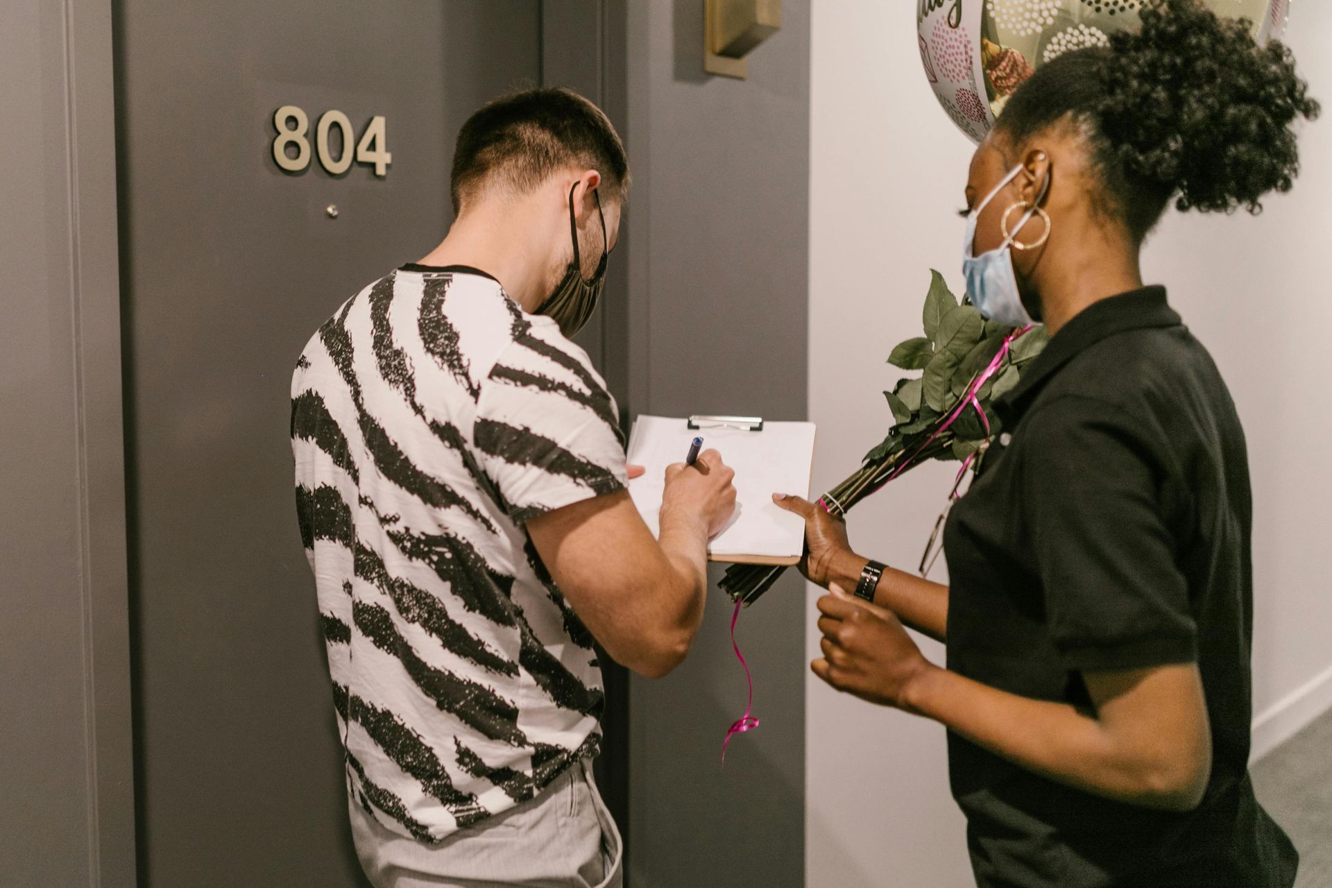 Person in zebra-print shirt signing for flowers delivered by a person holding them, at door 804.