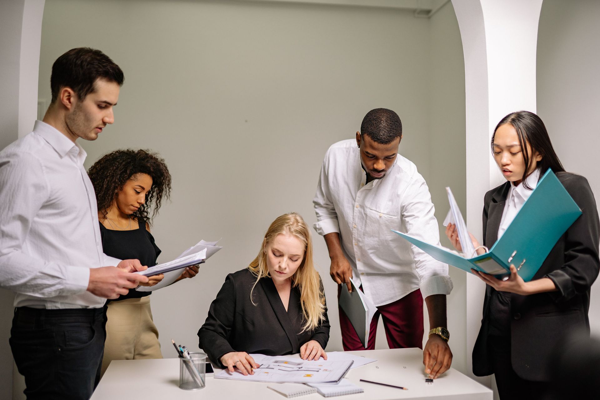 Five coworkers reviewing documents around a table in a bright office meeting room