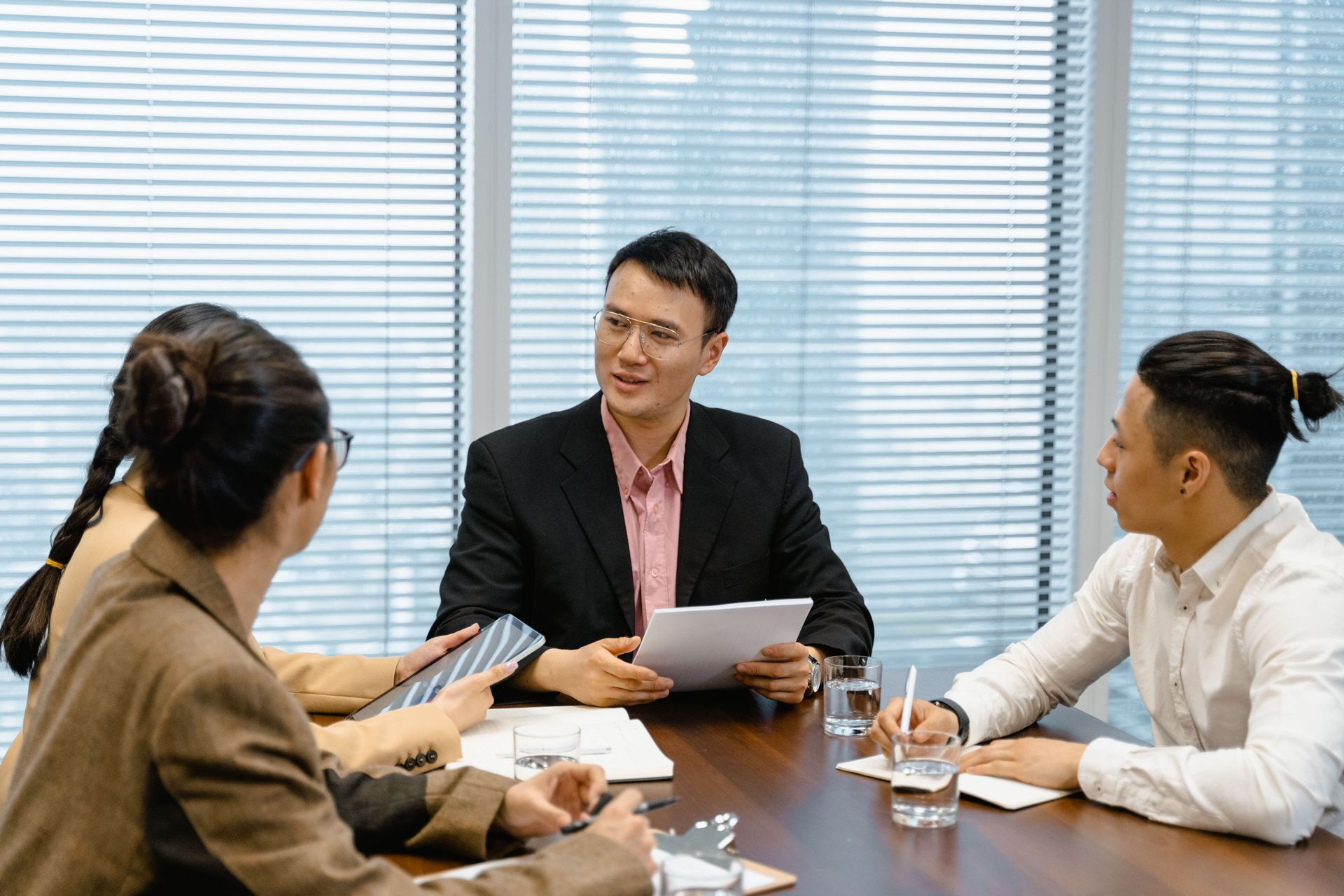 Three people in a meeting room discussing documents around a conference table.