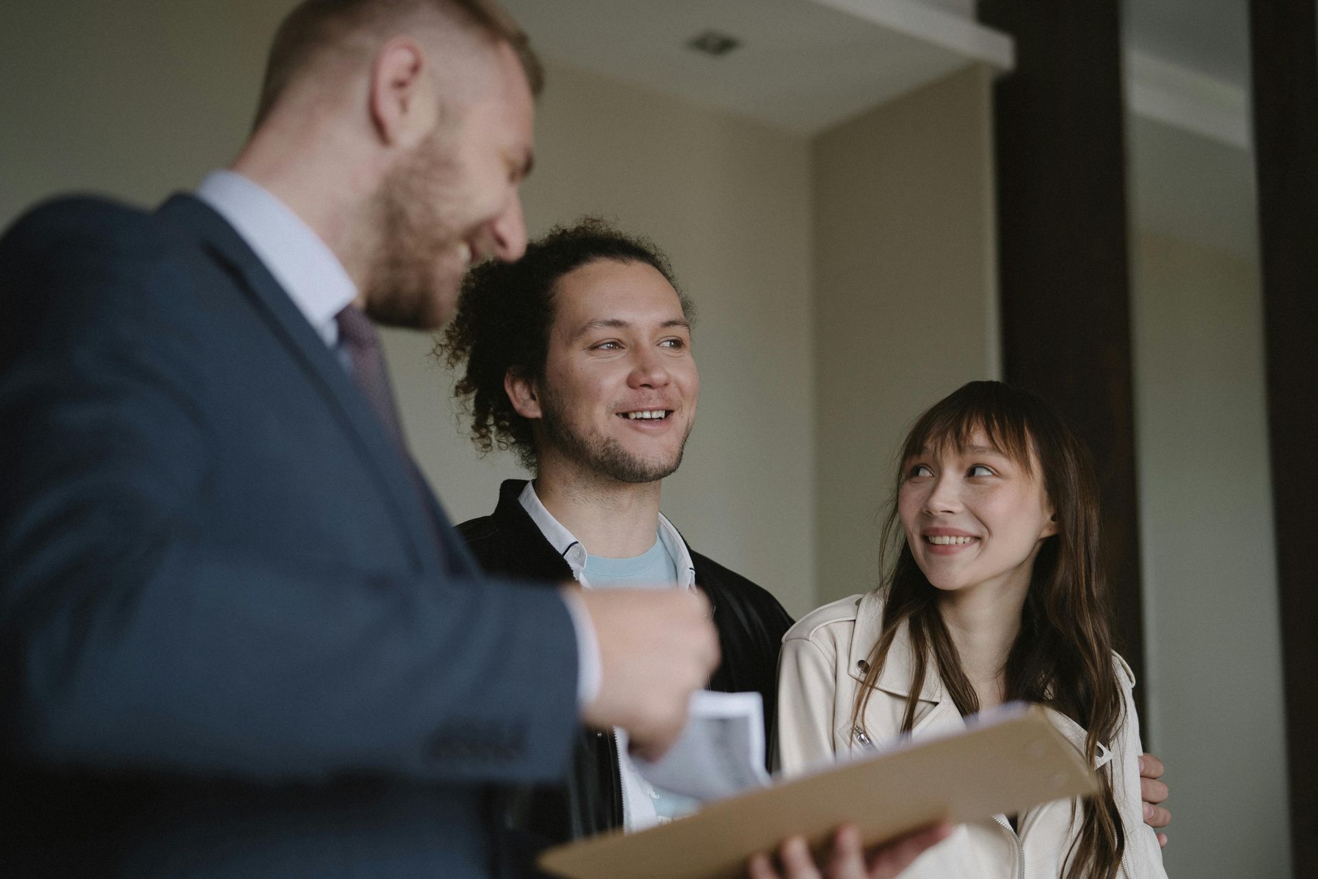 Real estate agent showing documents to smiling couple in a home.