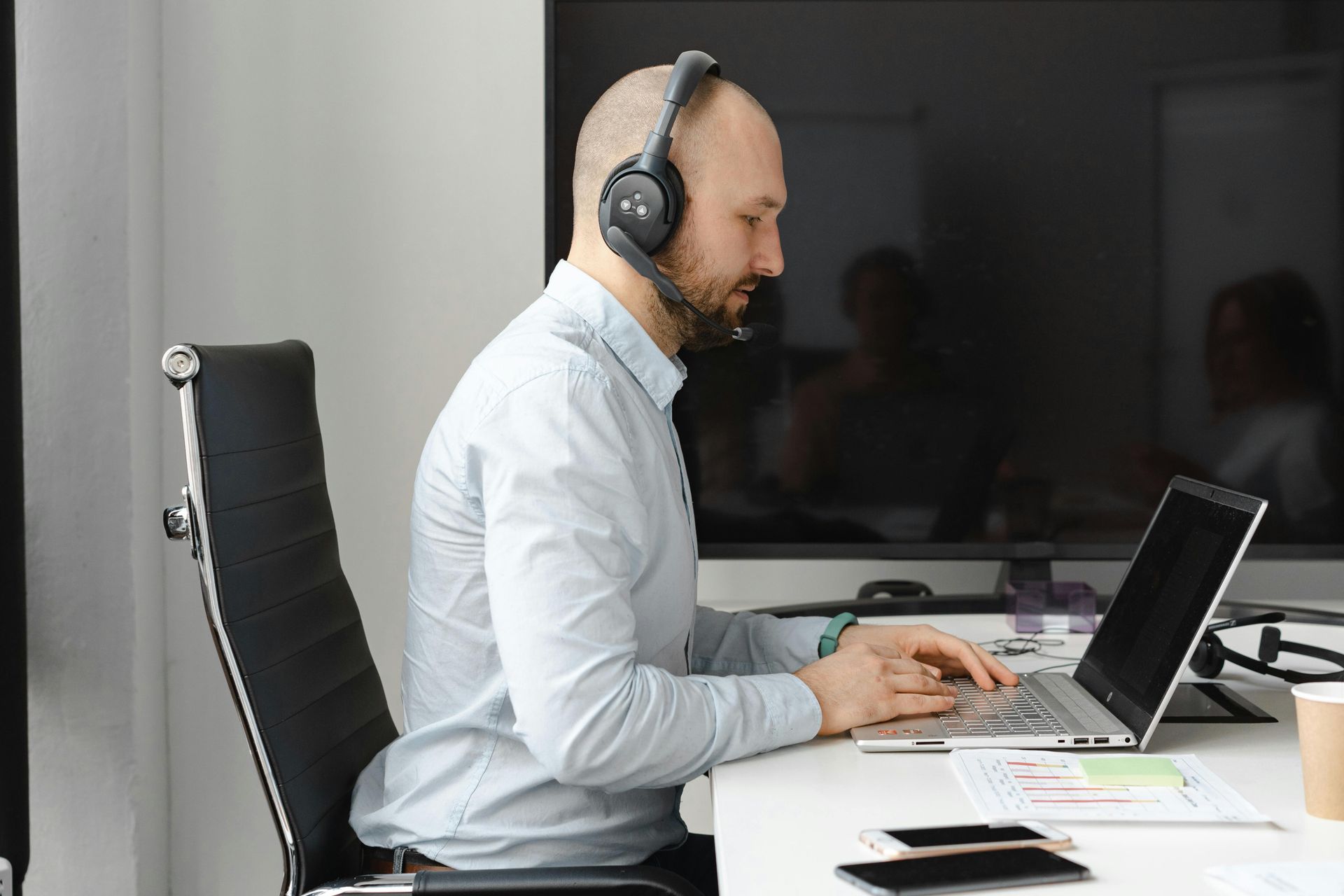 Man wearing headset, working on laptop at a desk in an office.