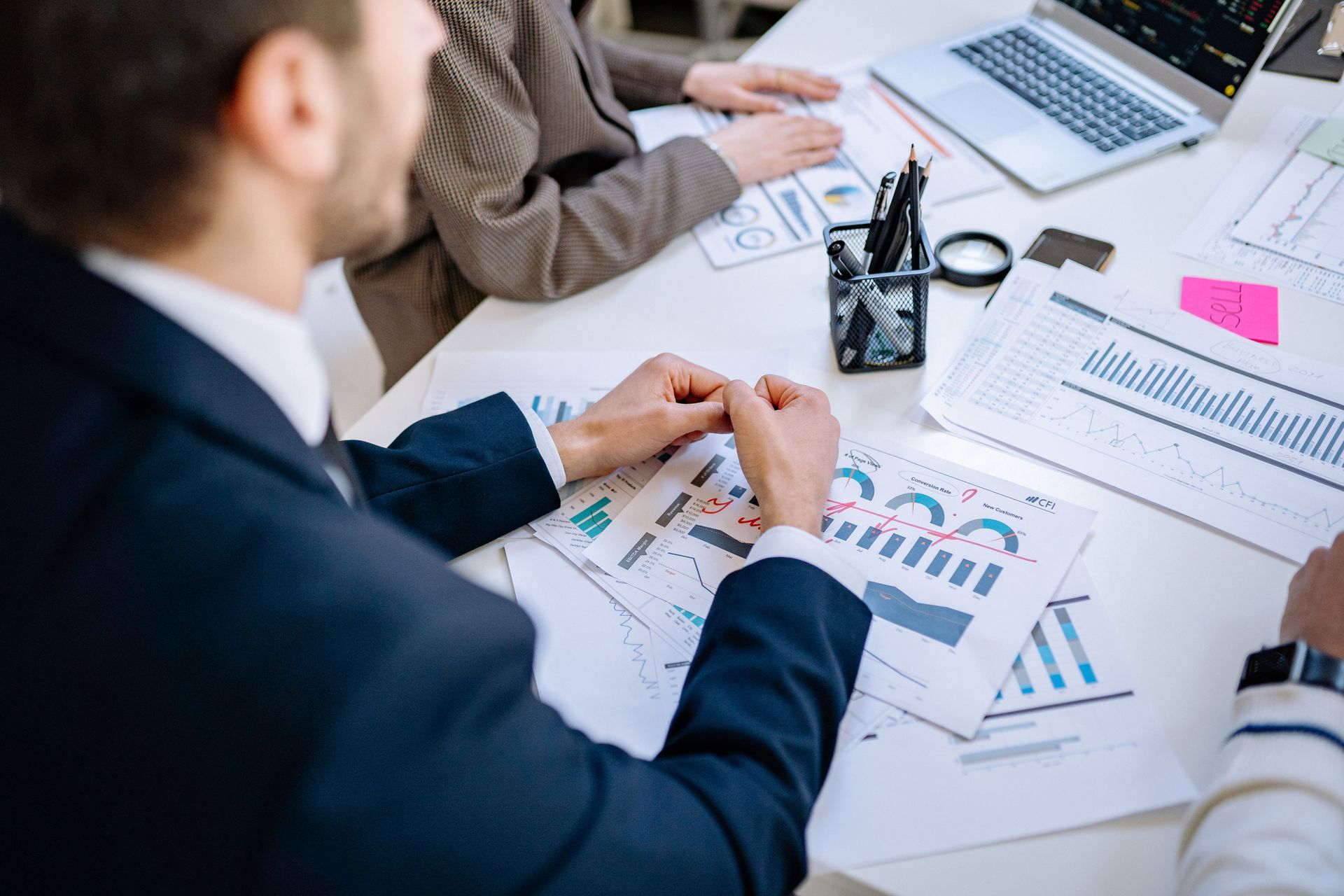 Business meeting with charts and laptop on a desk, hands reviewing printed reports and graphs.