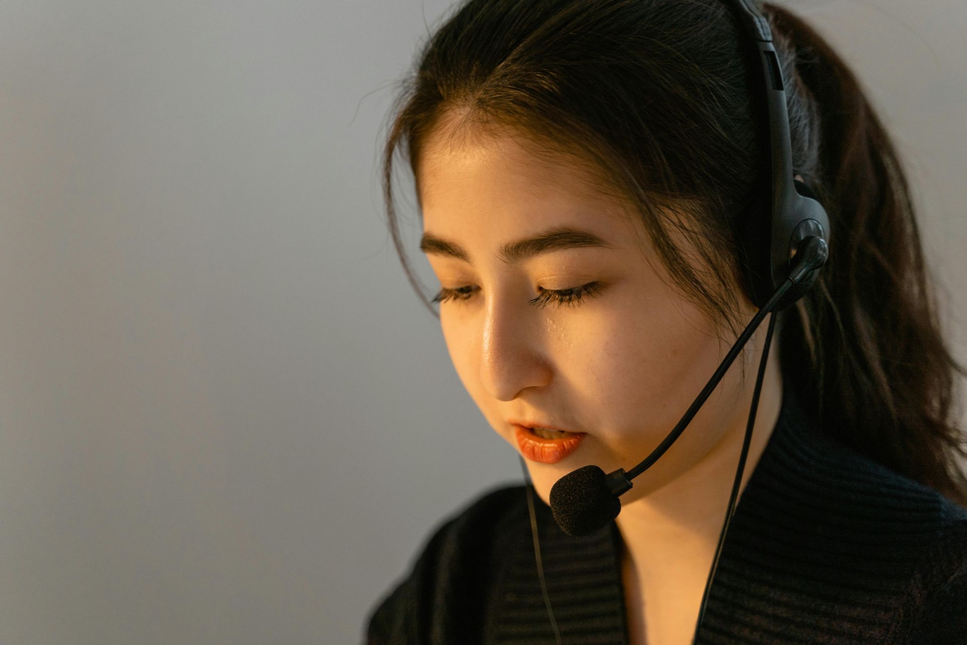 Woman wearing a headset, speaking, with her eyes lowered.