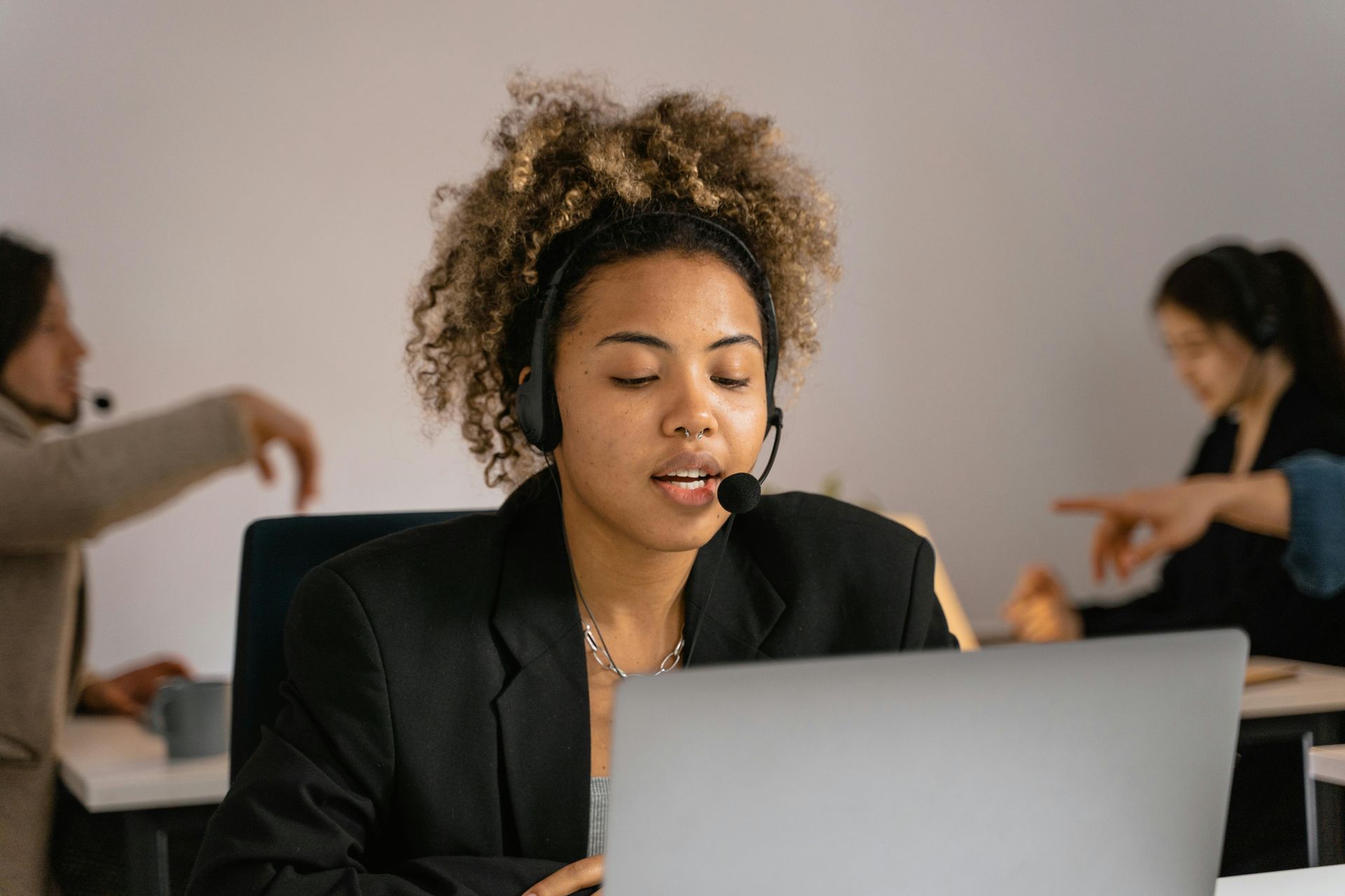 Woman with headset and laptop in office; talking, focused expression.