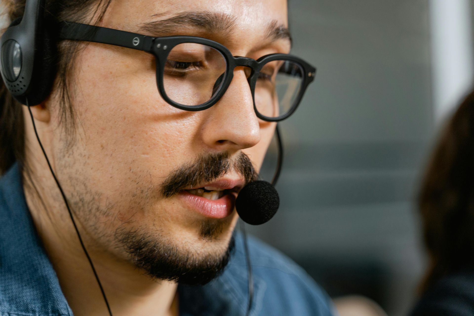 Man with glasses and headset speaking, close-up shot.