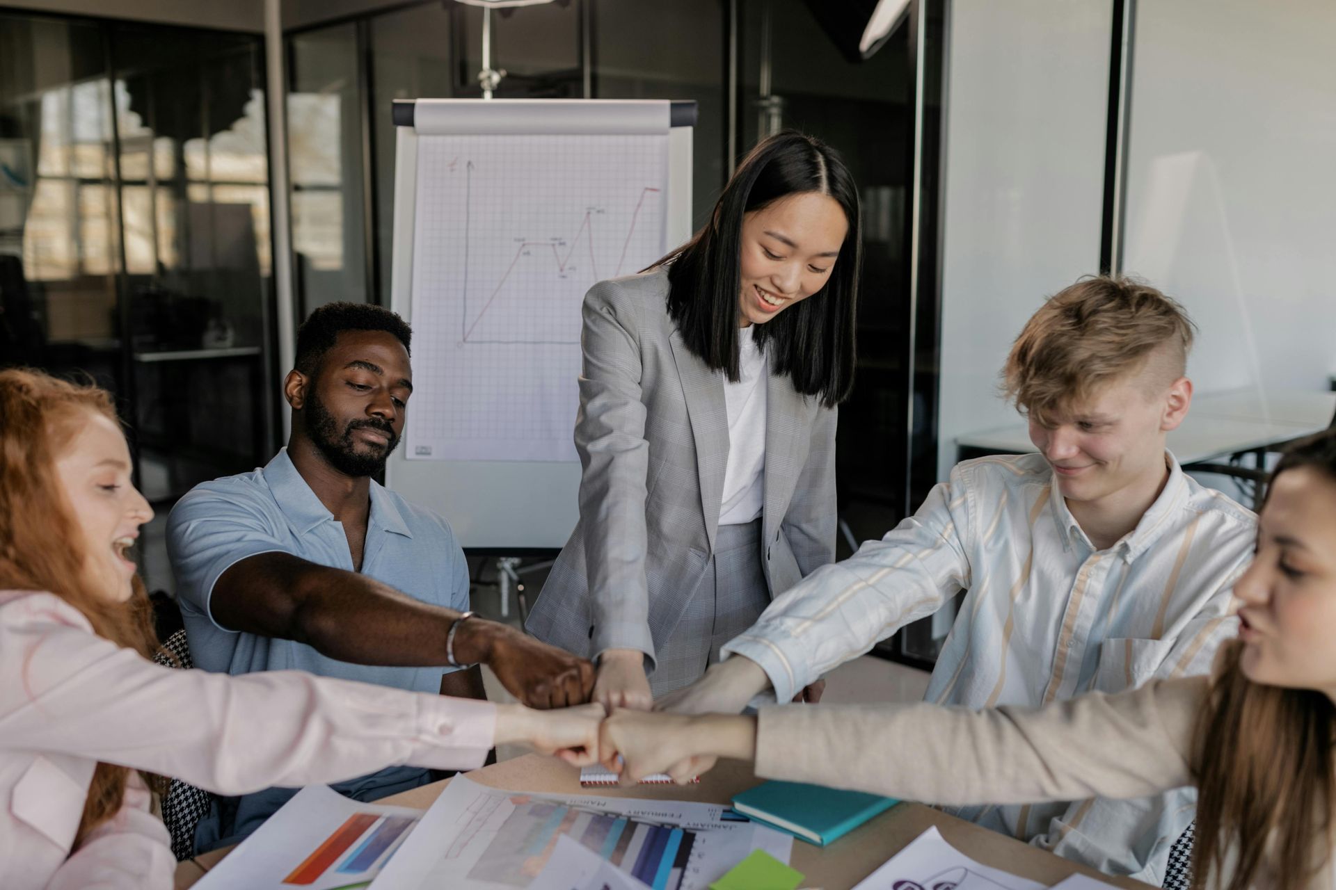 Team members in office, hands stacked together in unity, with a graph displayed.