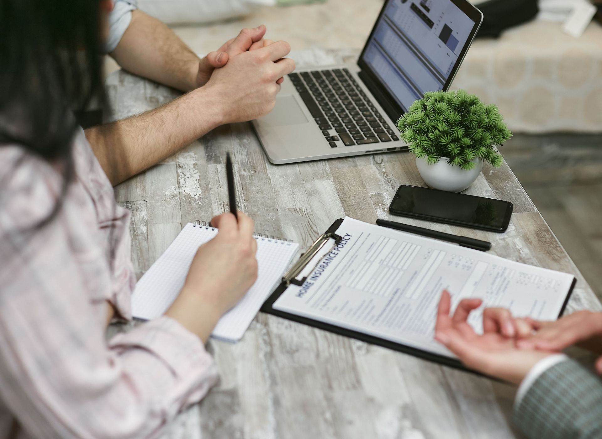 People taking notes and reviewing documents at a laptop during a meeting at a rustic table