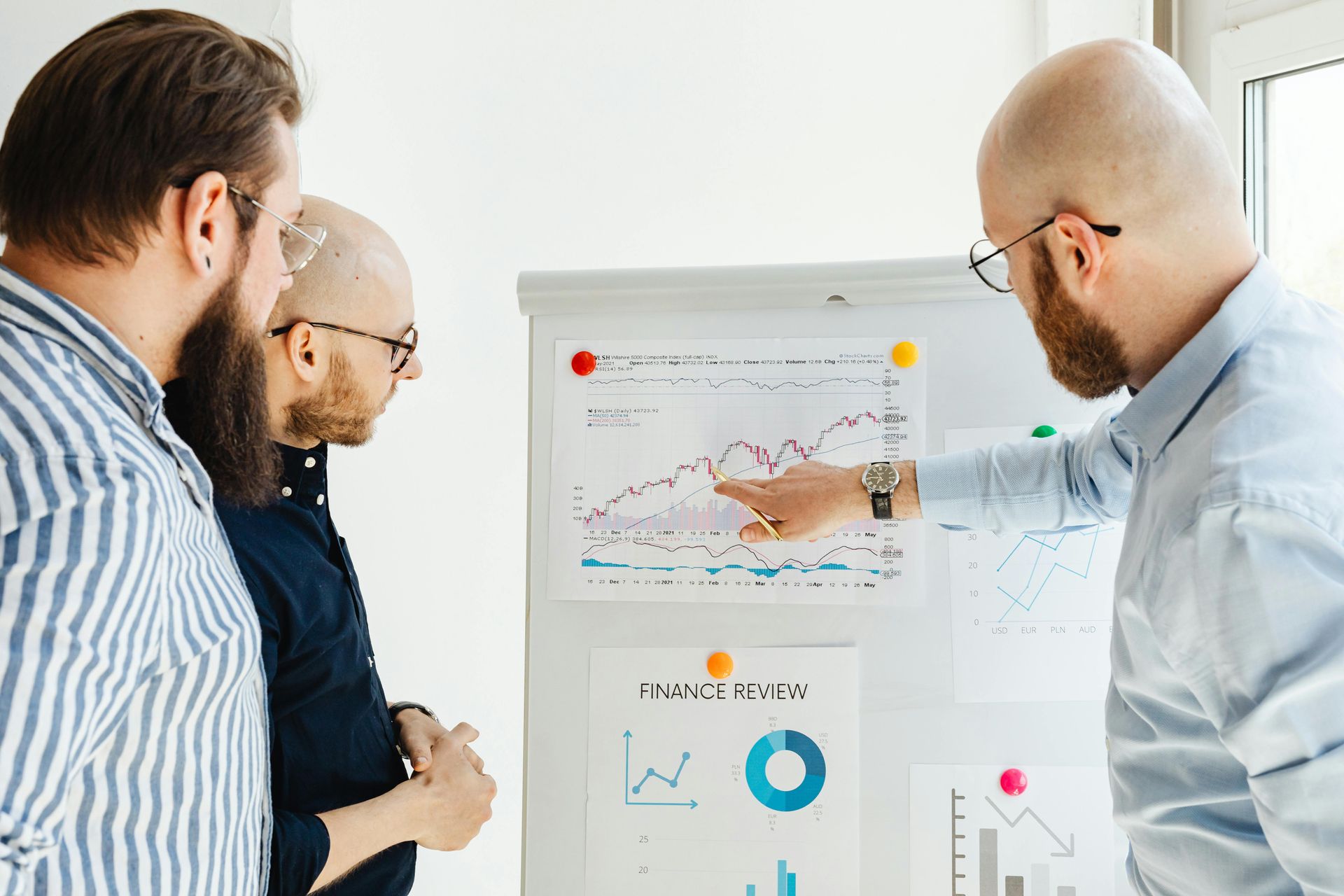 Three men in a bright office, reviewing a financial graph displayed on a whiteboard.