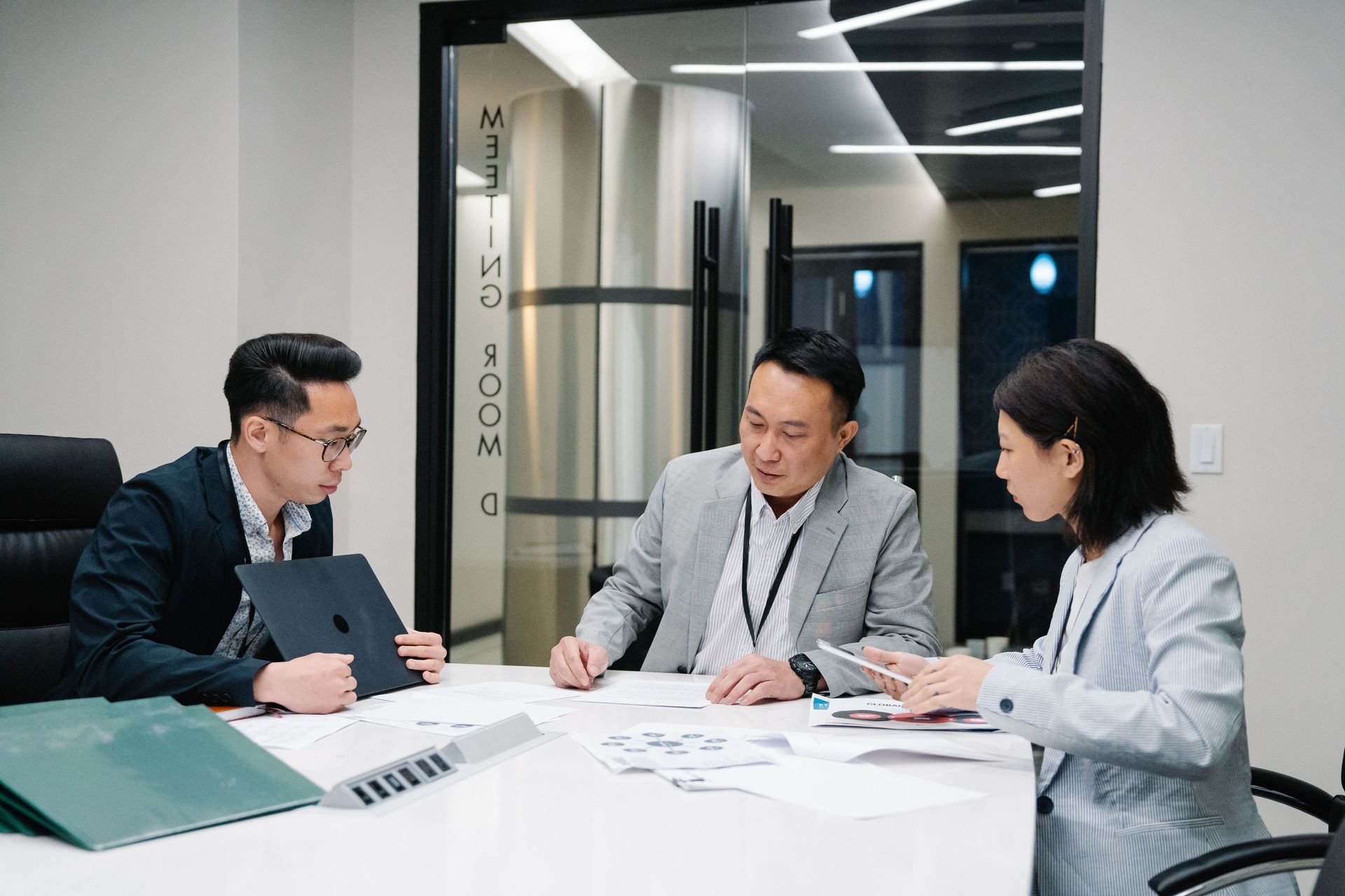 Three coworkers reviewing documents at a conference table in a glass-walled office