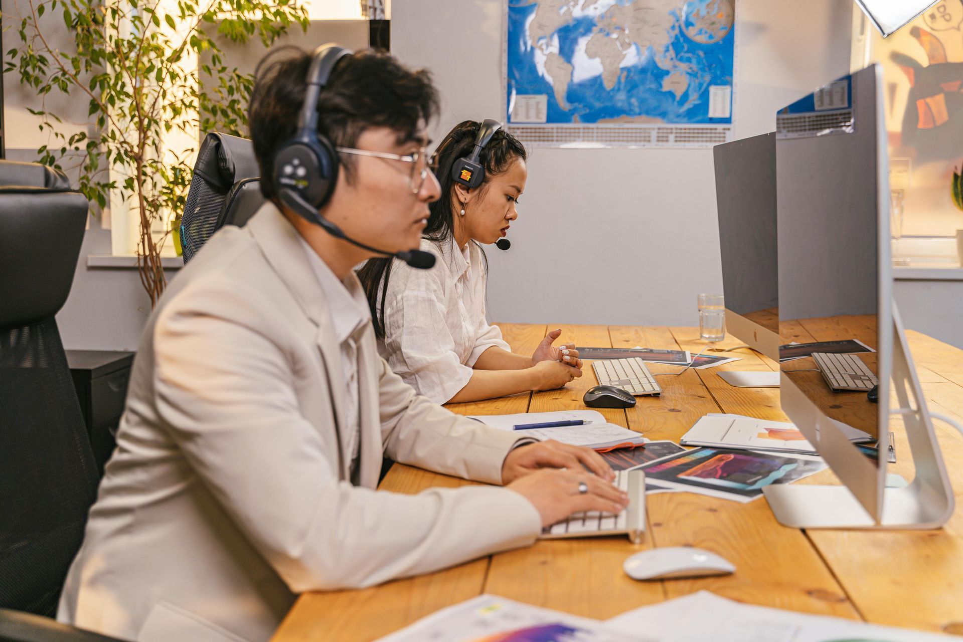 Two office workers wearing headsets work at computers in a professional setting.