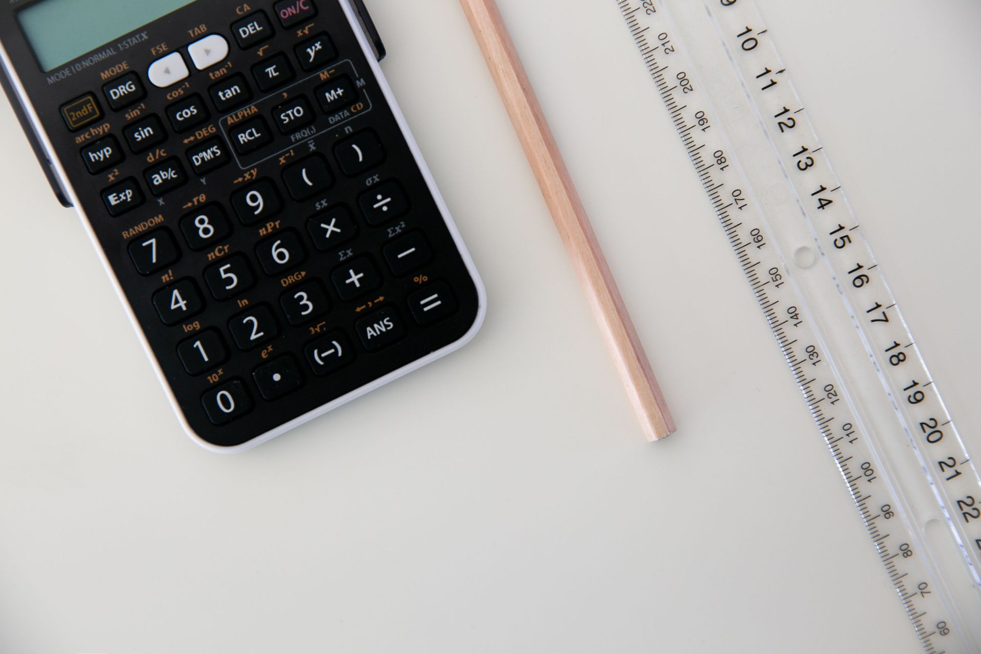 Calculator, pencil, and ruler on a white desk.