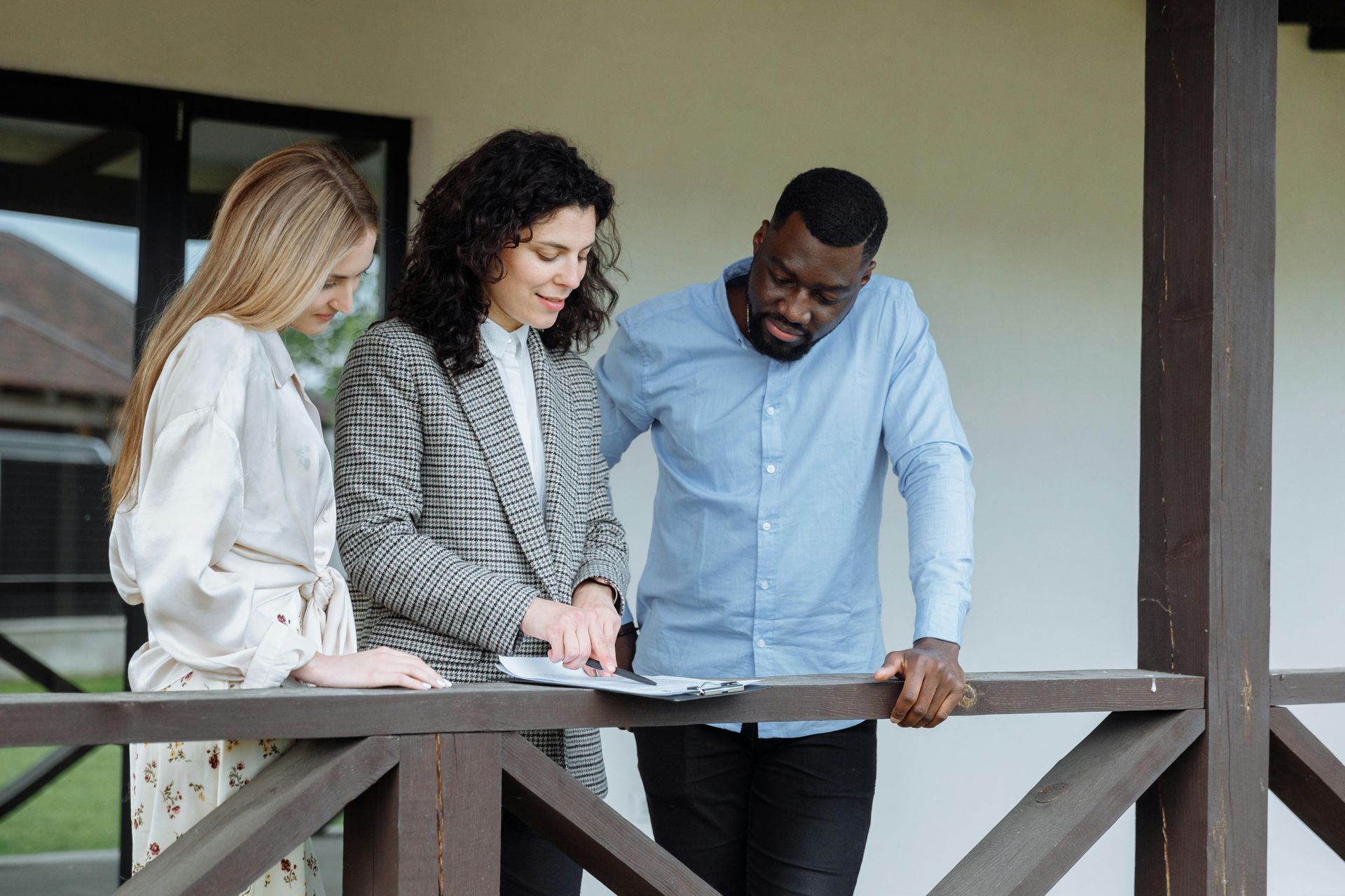 Three people stand on a porch, reviewing documents together in an outdoor, collaborative setting.