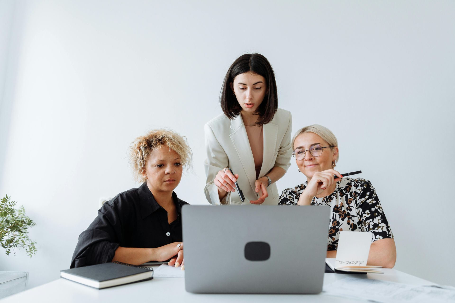 Three people collaborating at a table, looking at a laptop screen together in a bright office.