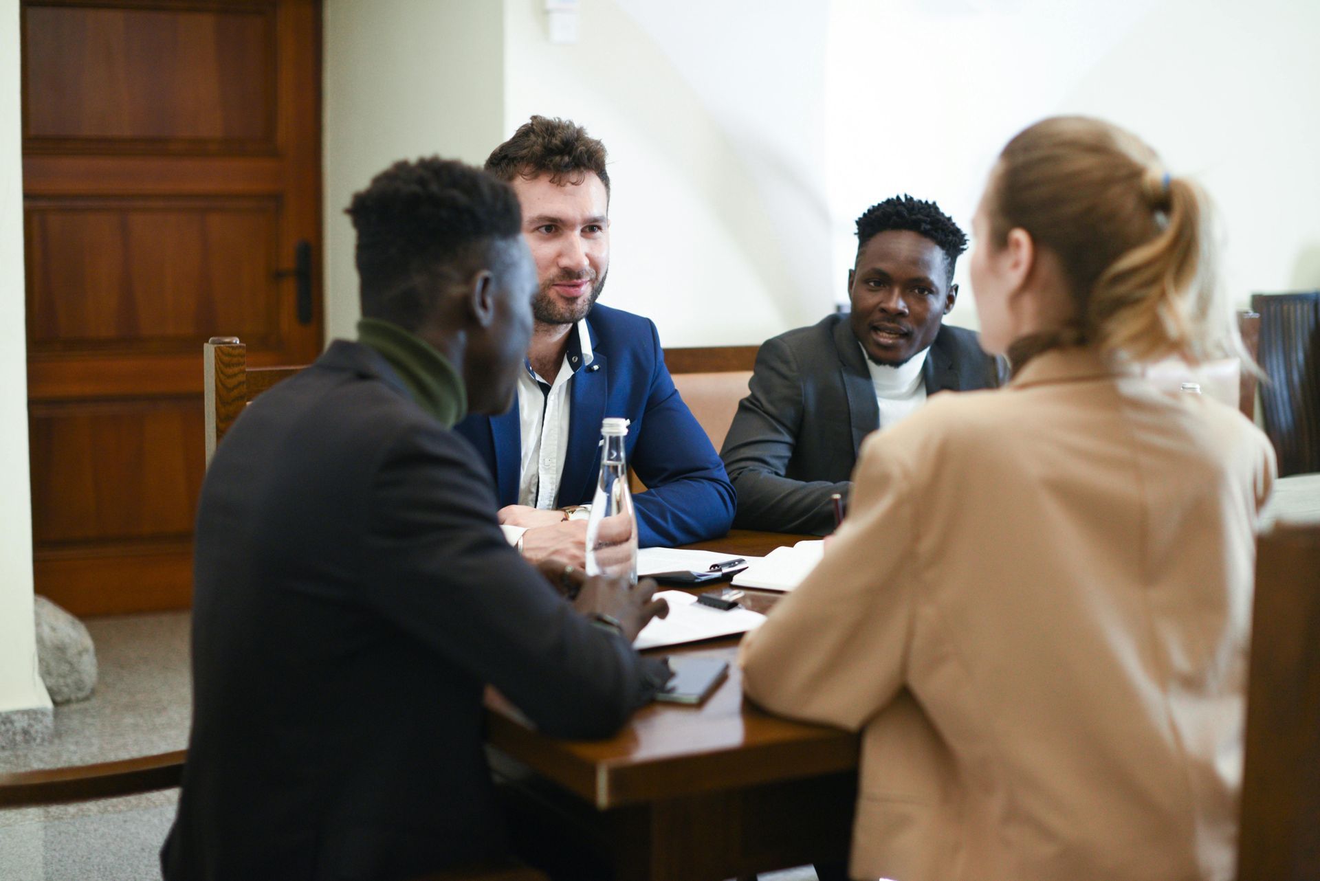Four professionals in business attire seated around a table, engaged in a discussion in an office setting.