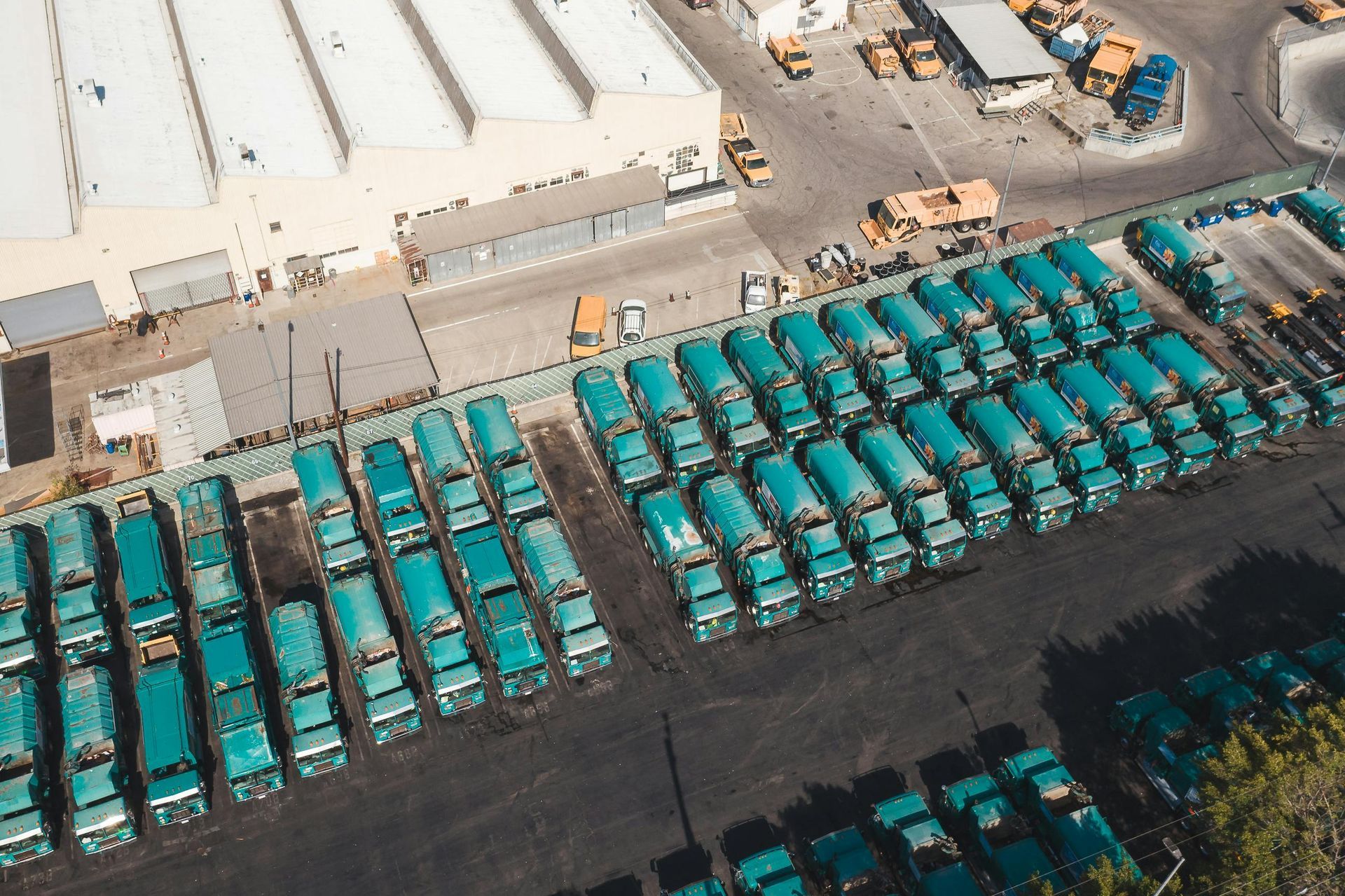 Aerial view of rows of teal trucks parked in a large lot next to a white industrial building.