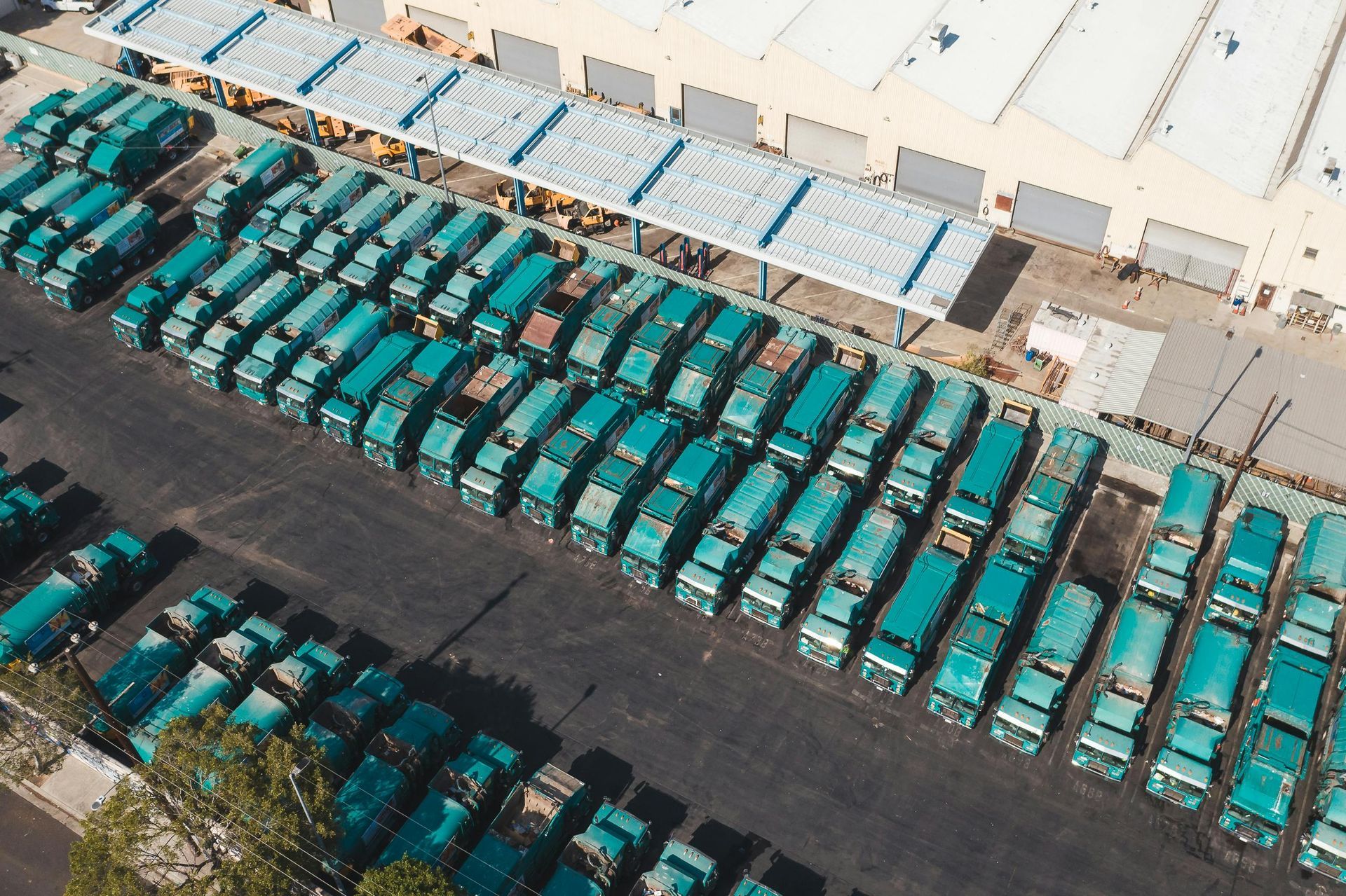 Aerial view of numerous teal-colored trucks parked in neat rows at a facility, beside a large building.