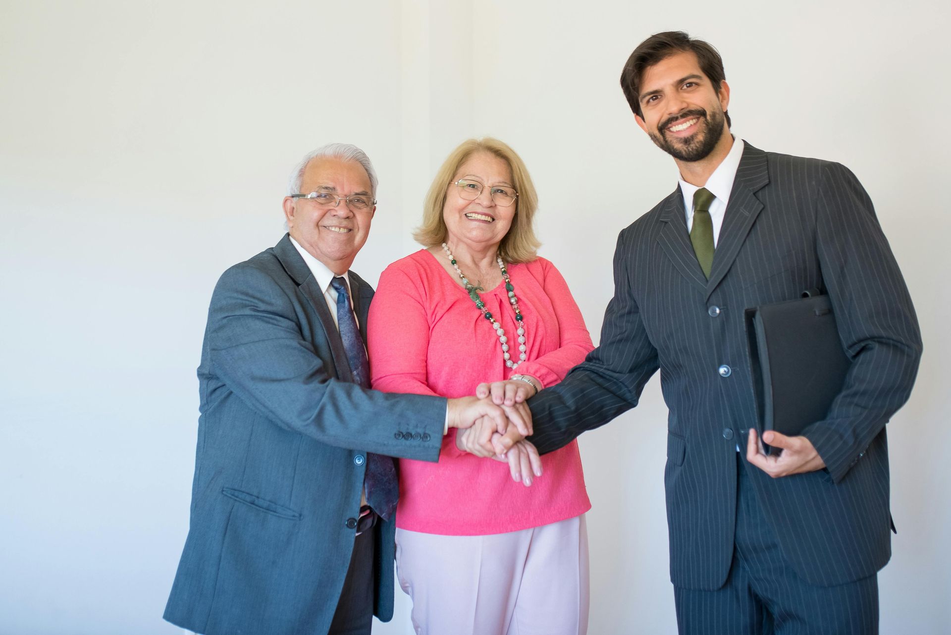 Man shaking hands with older couple; they are smiling in an office setting.