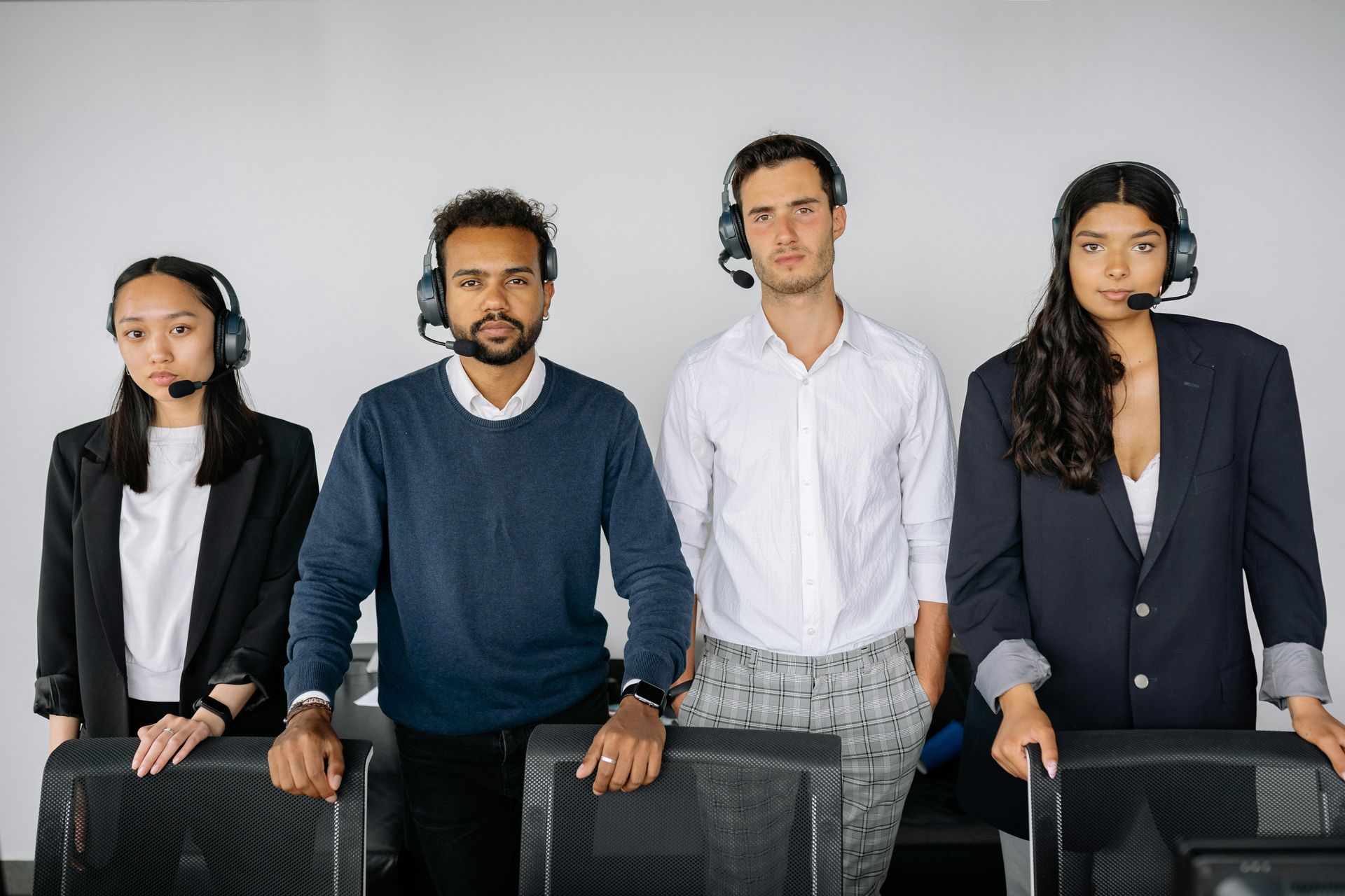 Four people wearing headsets stand behind office chairs in a brightly lit, minimalist office space.
