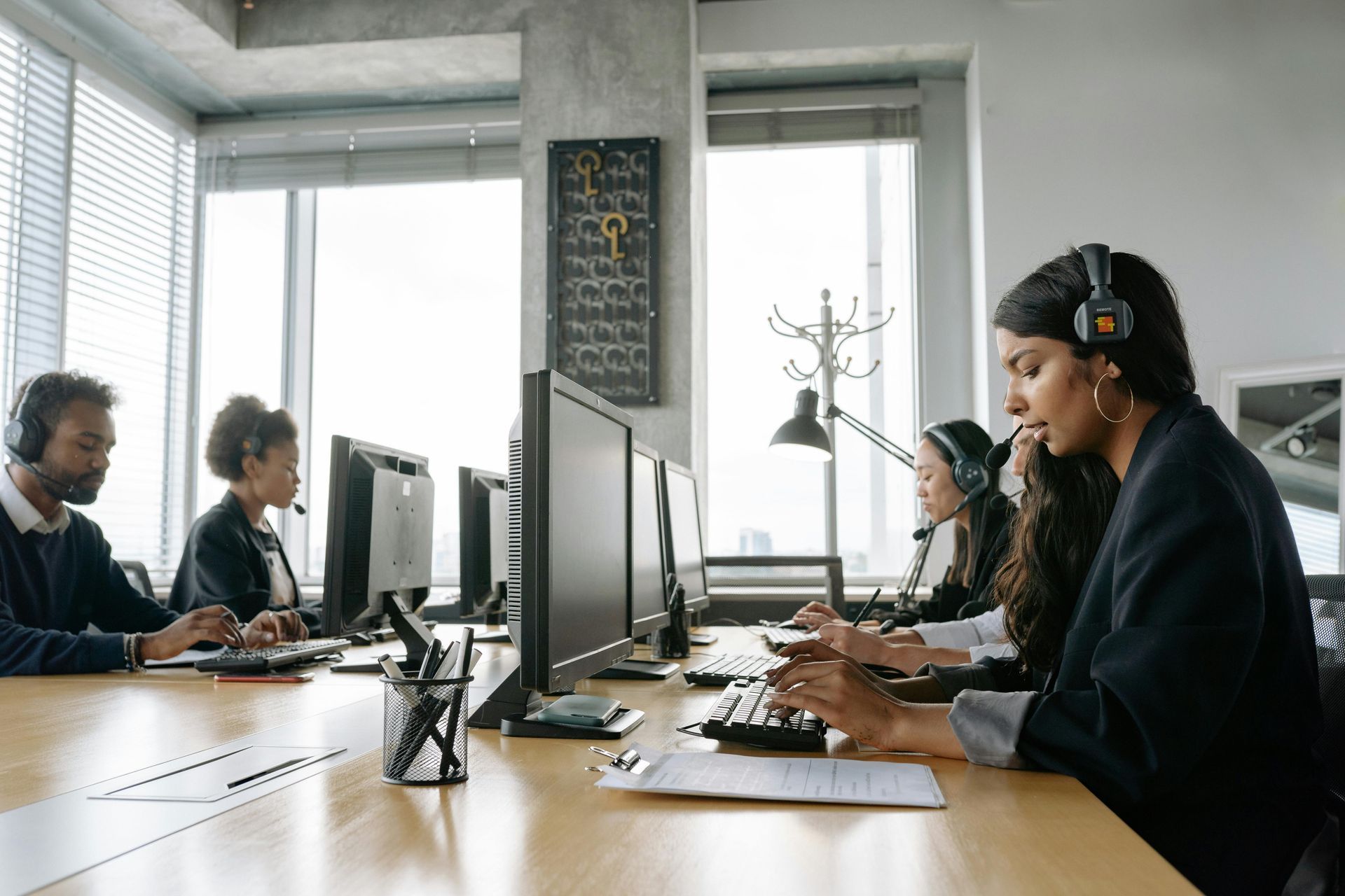 People working at computers in an office setting, wearing headsets.
