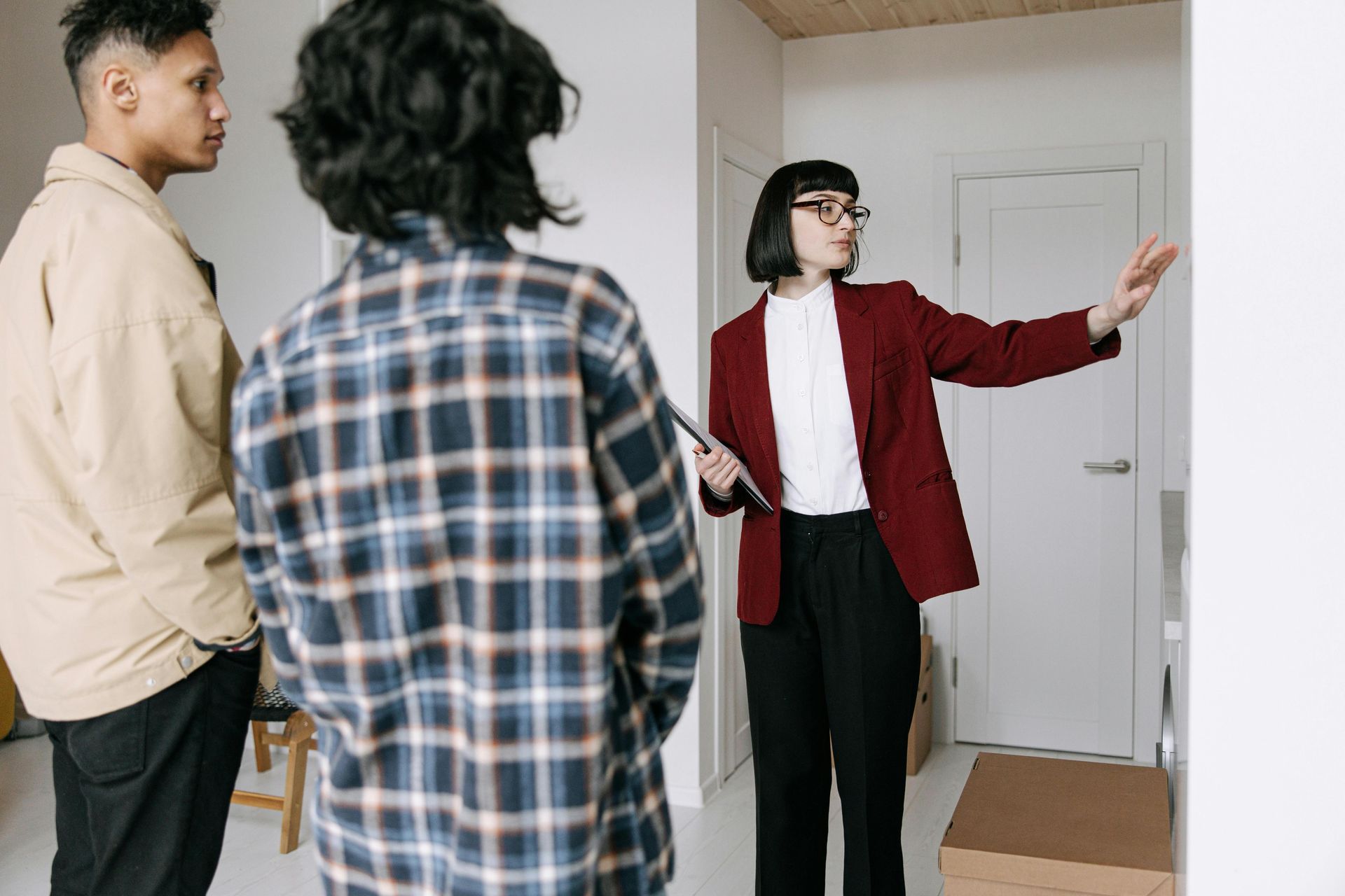 Real estate agent showing a couple a room, gesturing. White walls, indoor setting.