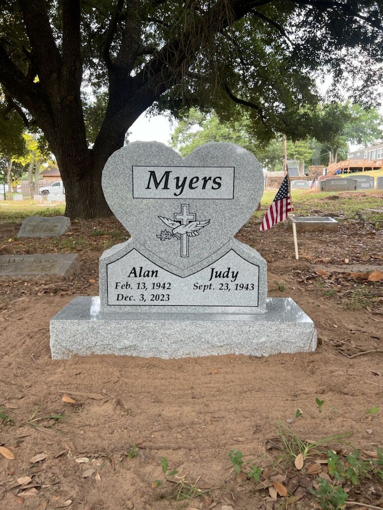 A gravestone in the shape of a heart with a cross on it in a cemetery.