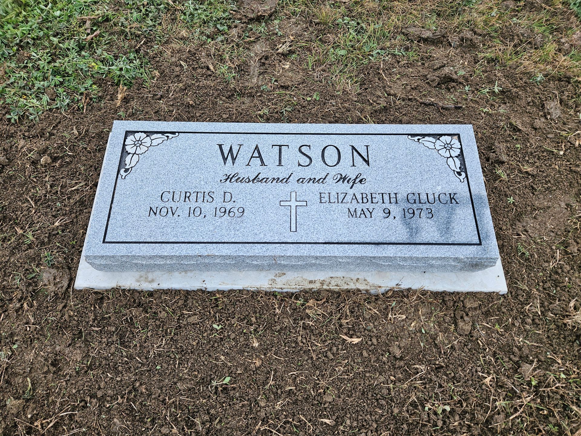 A gravestone for a man named watson is sitting in the grass.