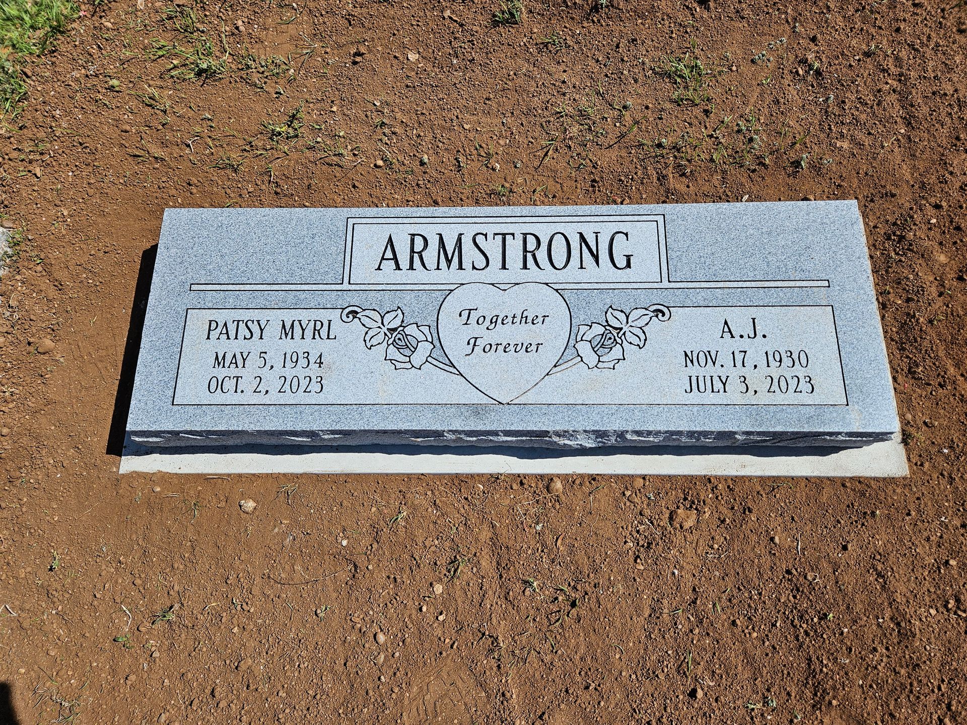 A gravestone for armstrong is sitting in the dirt in a graveyard.