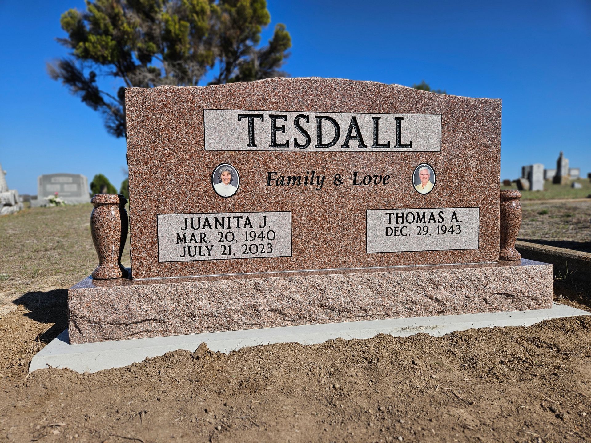 A gravestone for a family in a cemetery with a tree in the background.