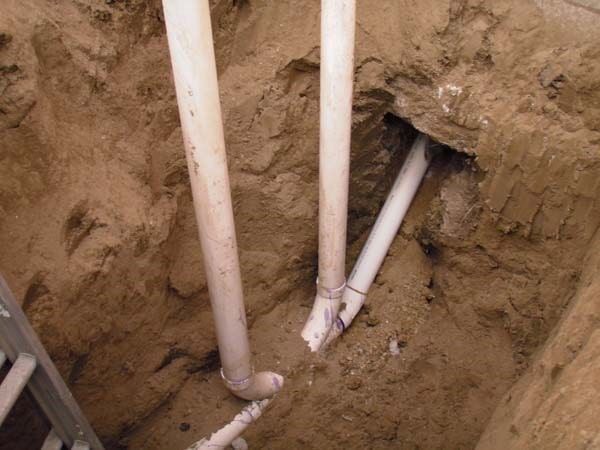 Two white pipes are laying in the dirt in a hole.