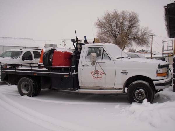 A white truck with a red tank on the back is parked in the snow