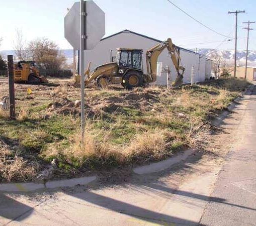 A bulldozer is digging a hole in the grass in front of a white building.