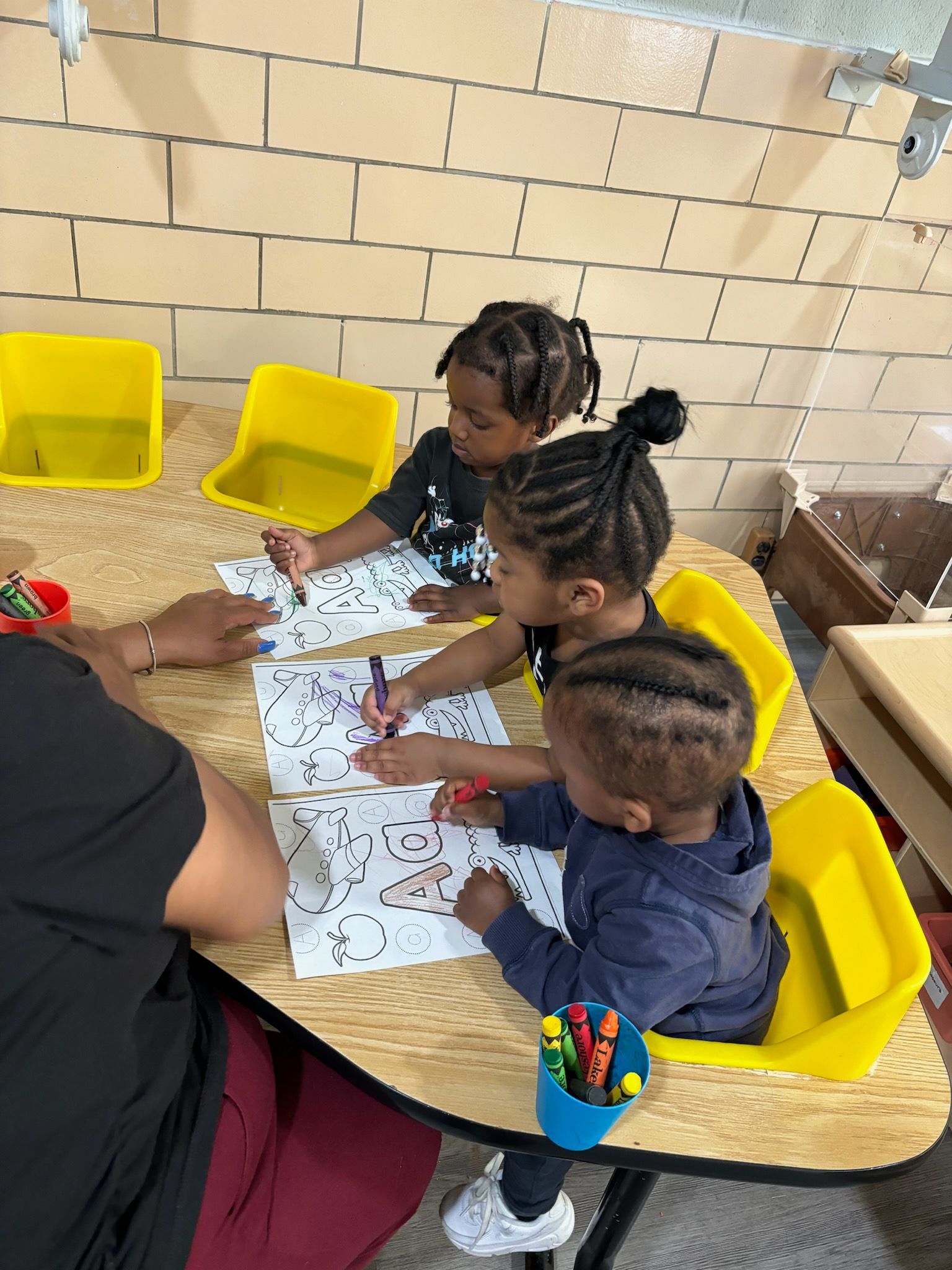 A group of children are sitting at a table drawing with crayons.