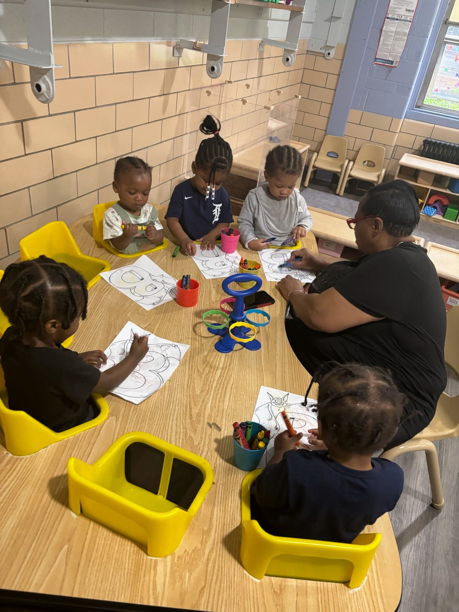 A group of children are sitting around a table with a teacher.