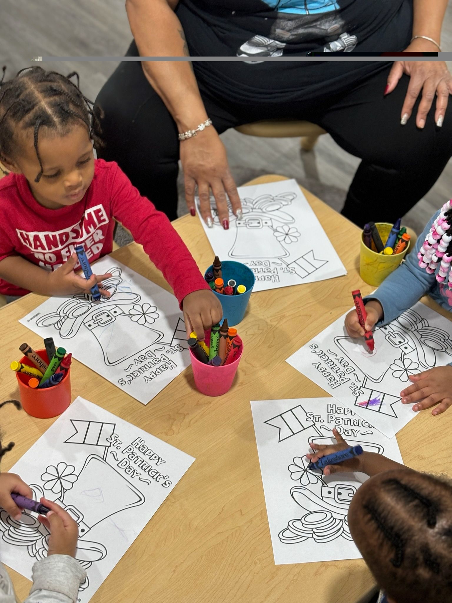 A group of children are sitting around a table drawing with crayons.