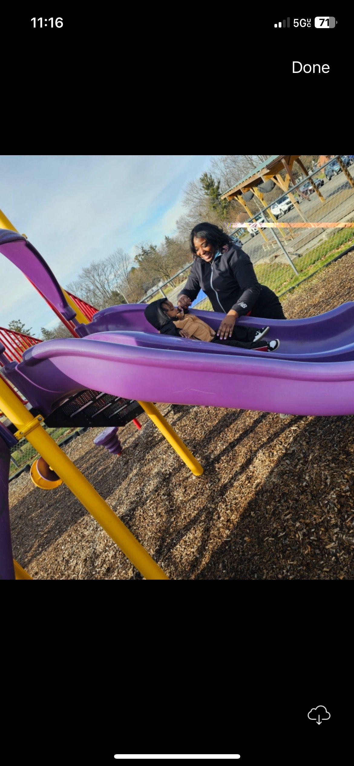 A woman is playing with a child on a slide at a playground.