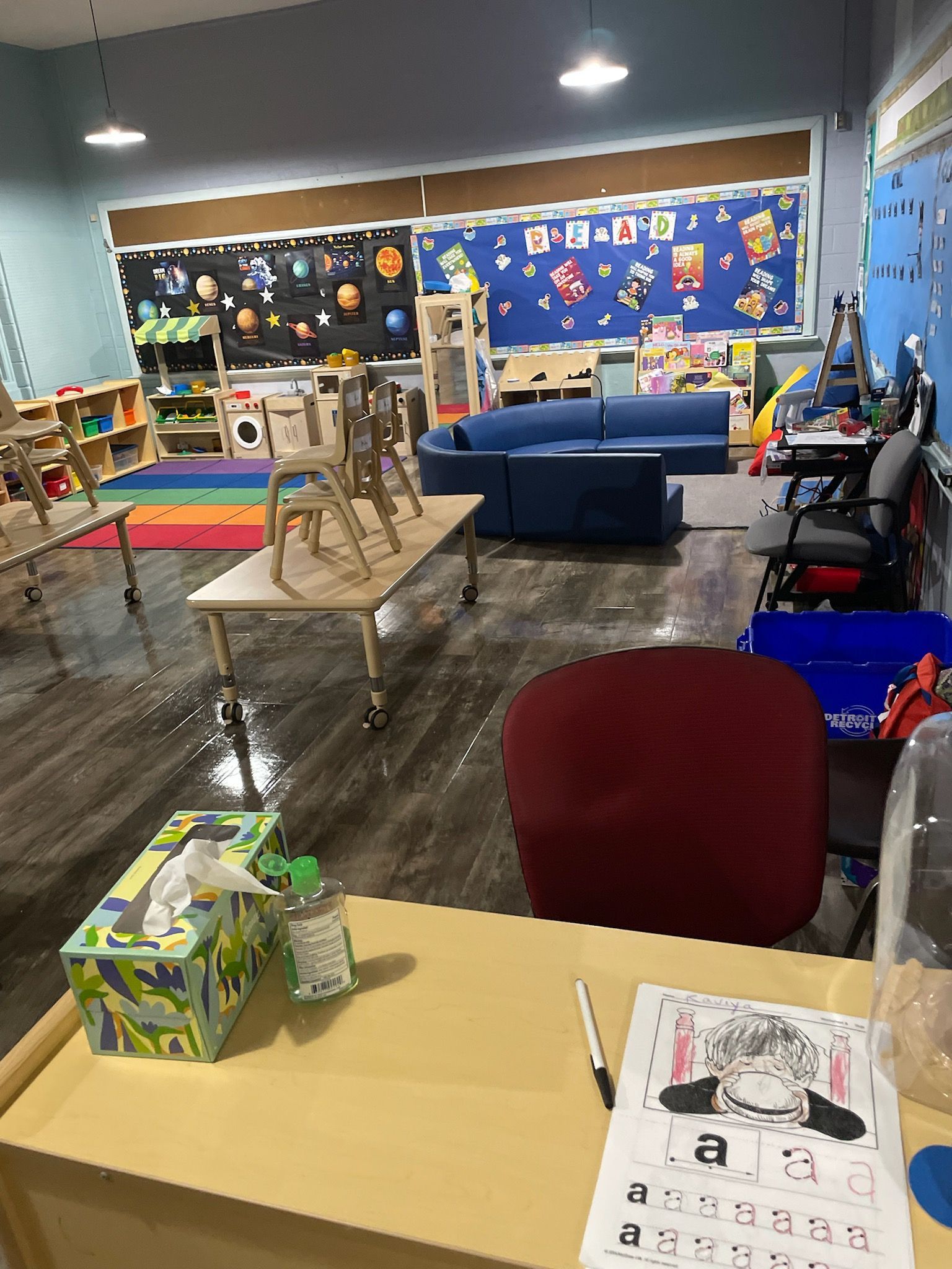 A classroom with chairs stacked on top of each other and a desk with a pen on it.