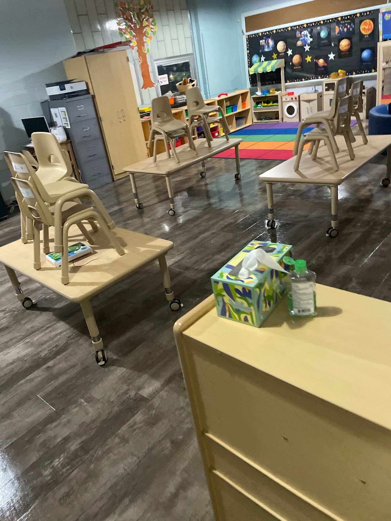 A classroom with tables and chairs and a box of tissues on a table.