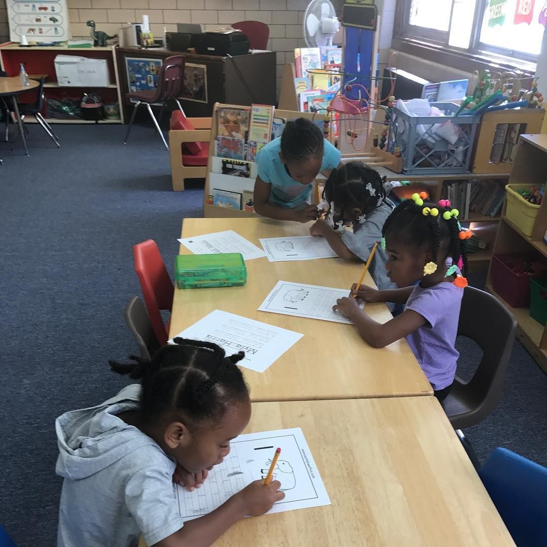 A Group of Children Are Sitting at Tables in A Classroom Writing on Paper