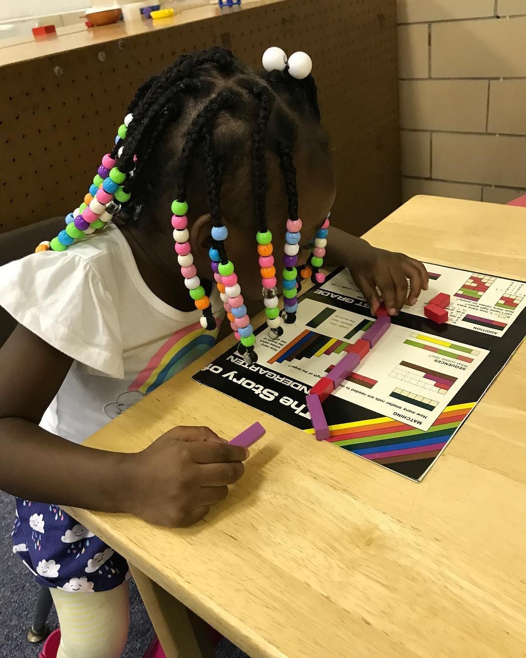 A Little Girl with Braids Is Sitting at A Table Playing with Toys