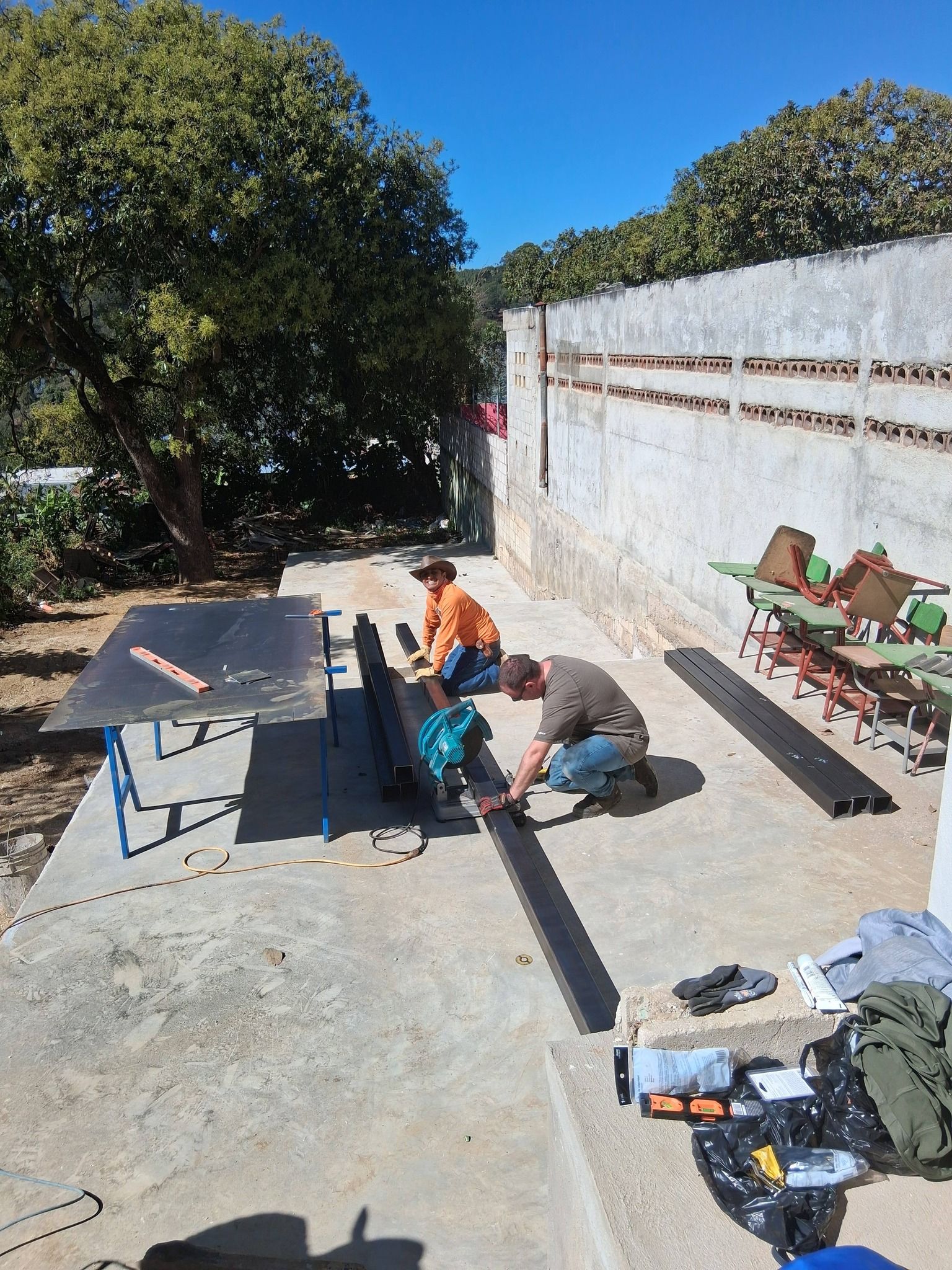 Two people work on a project outside on a concrete surface. One kneels, the other sits.